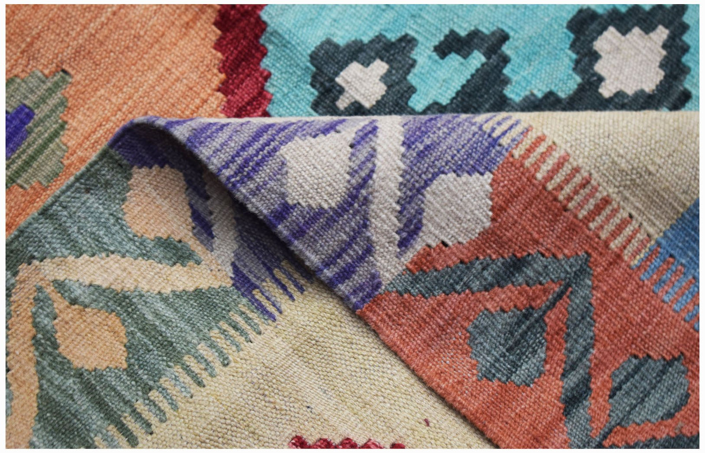 A folded Afghan Maimana kilim rug featuring colorful geometric patterns in a flatweave wool texture.