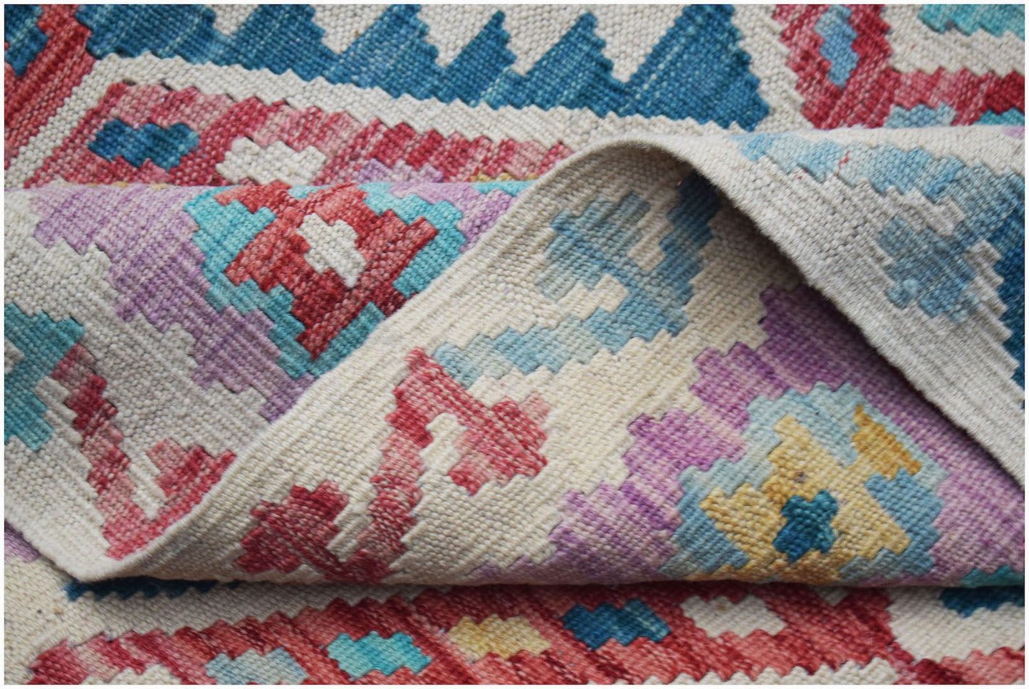 A handwoven Afghan Maimana kilim rug featuring a colorful geometric pattern on a cream background.