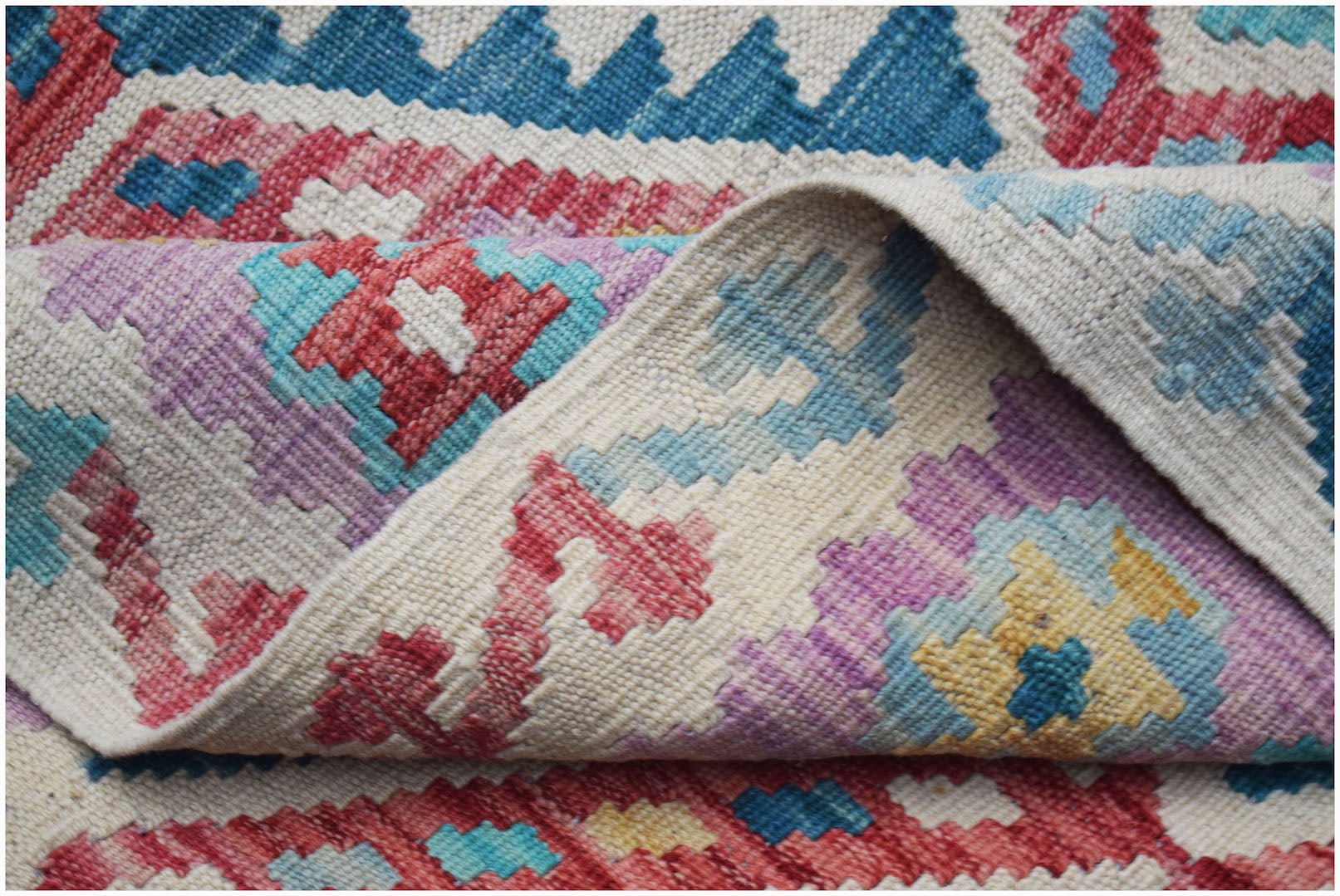 A handwoven Afghan Maimana kilim rug featuring a colorful geometric pattern on a cream background.