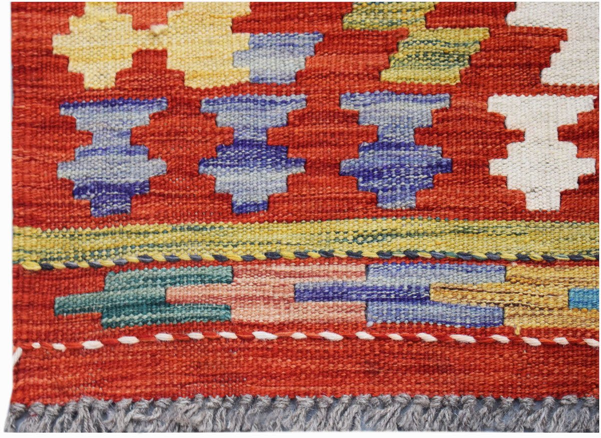 Handwoven Afghan Maimana kilim featuring geometric patterns in vibrant colors on a red background.