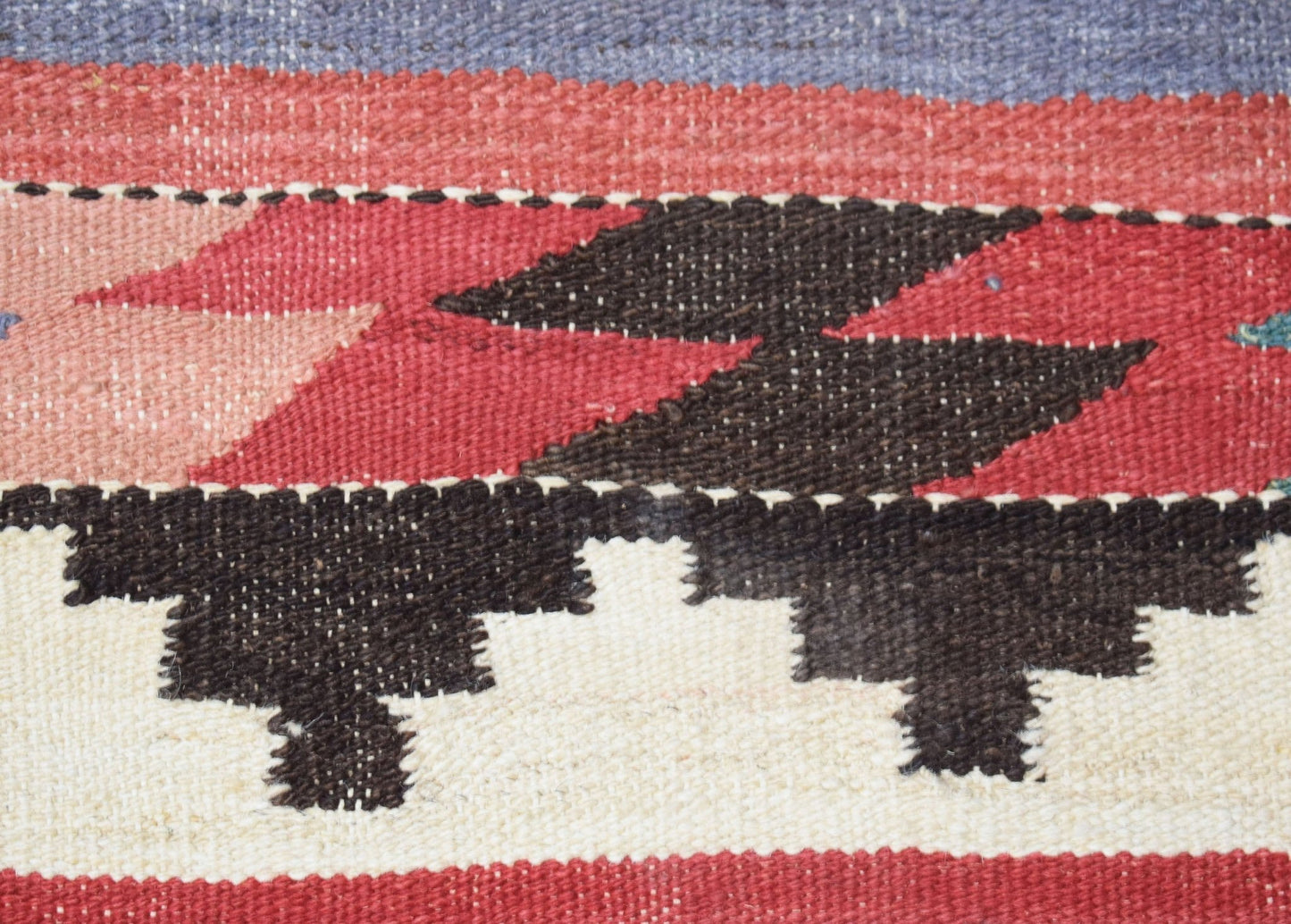 A close-up of a handmade Afghan Maimana kilim featuring geometric patterns in red, black, and cream.