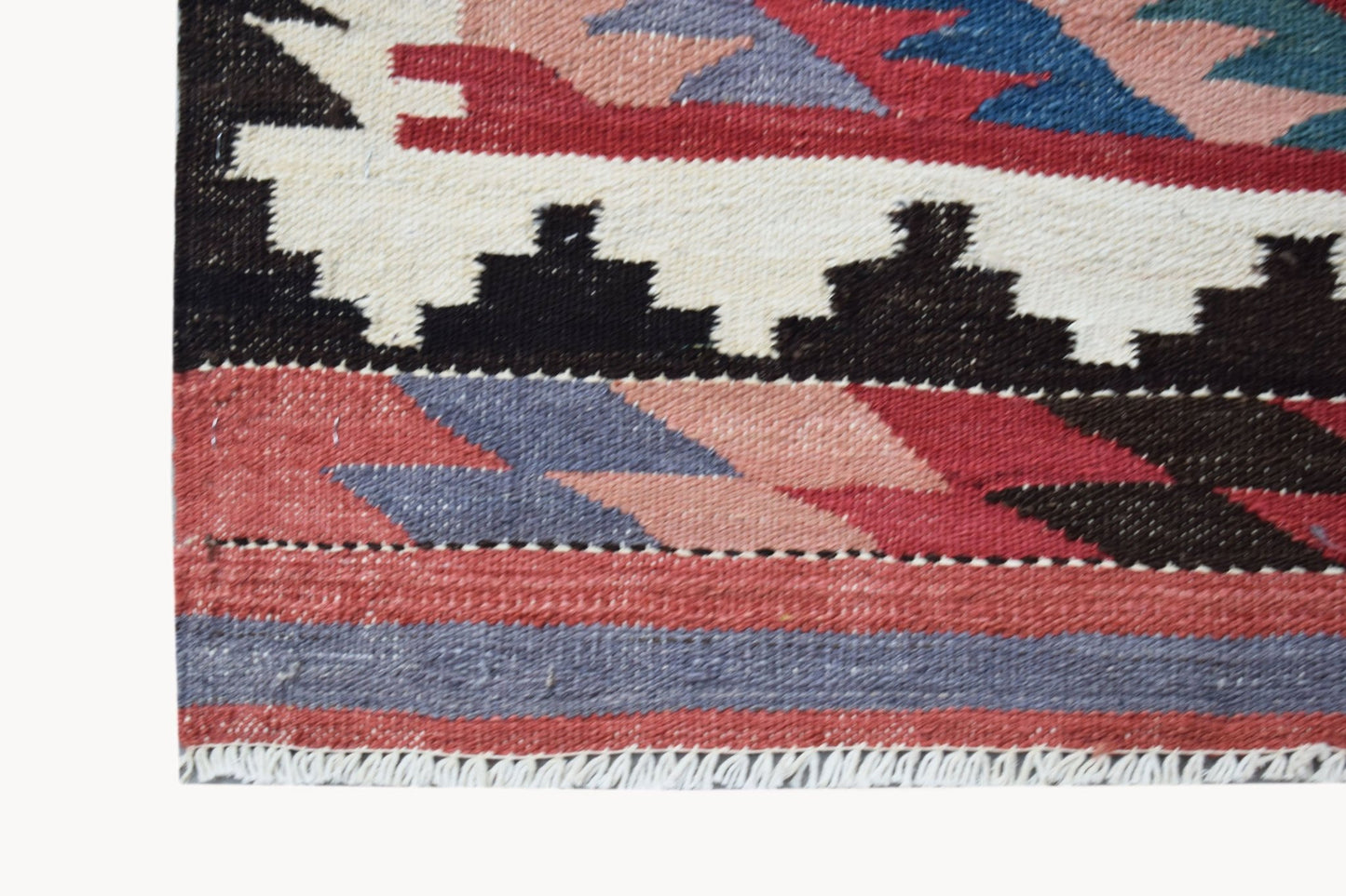 A close-up of a handmade Afghan Maimana kilim featuring geometric patterns in red, blue, and cream.
