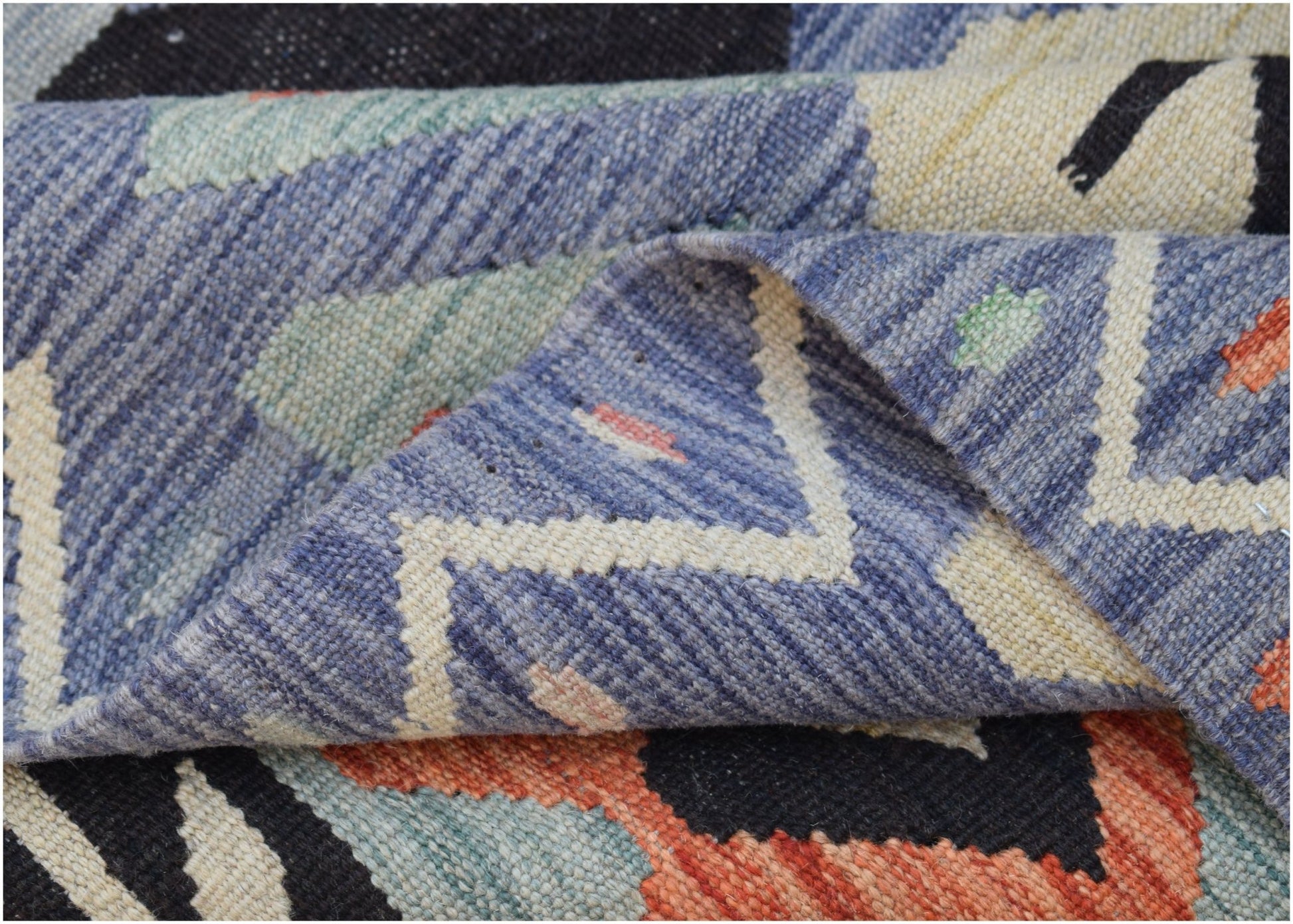 A close-up of a handwoven Afghan Maimana kilim featuring a geometric pattern in wool.