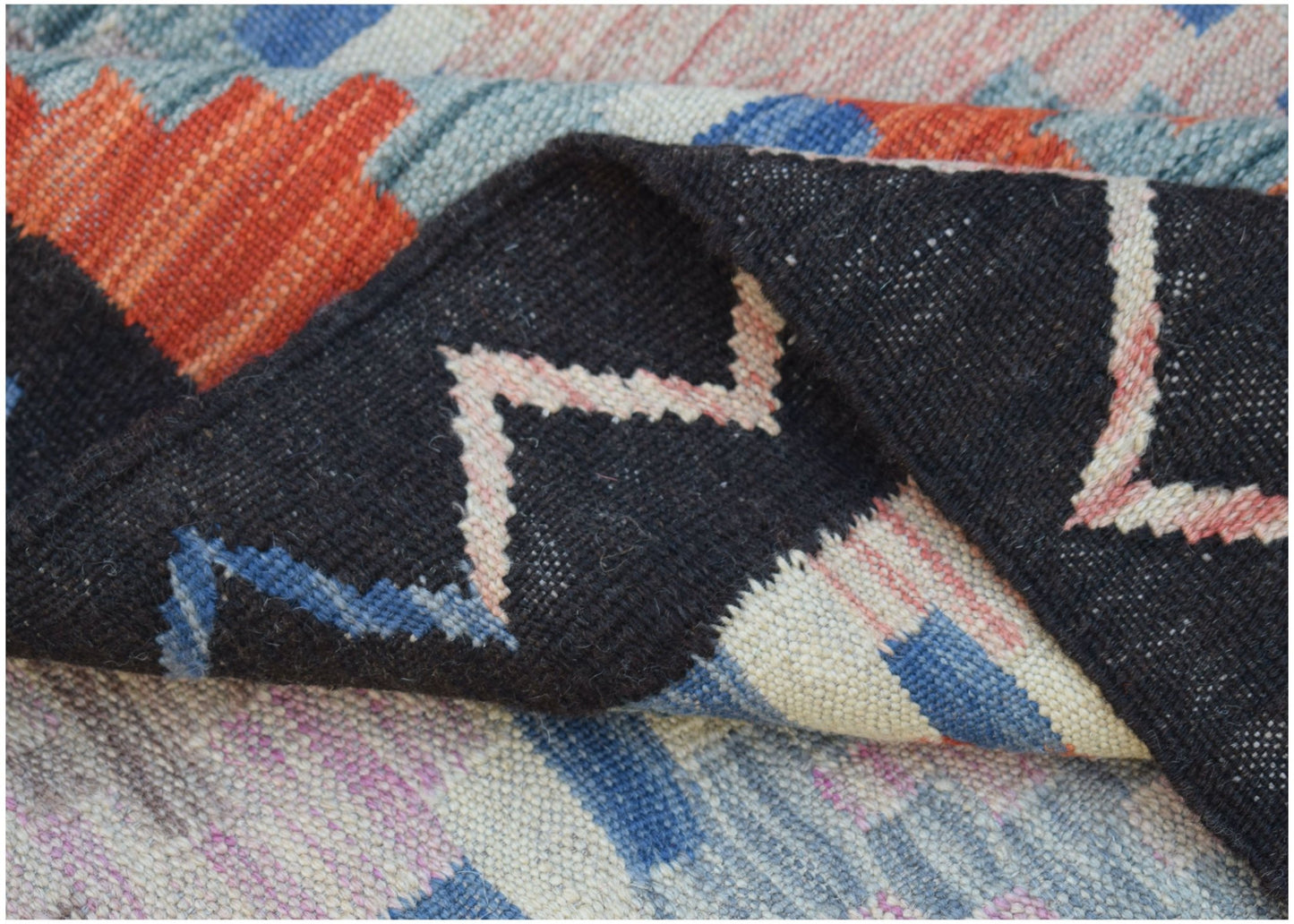 A folded Afghan Maimana kilim rug featuring a geometric pattern in black, blue, and orange wool.
