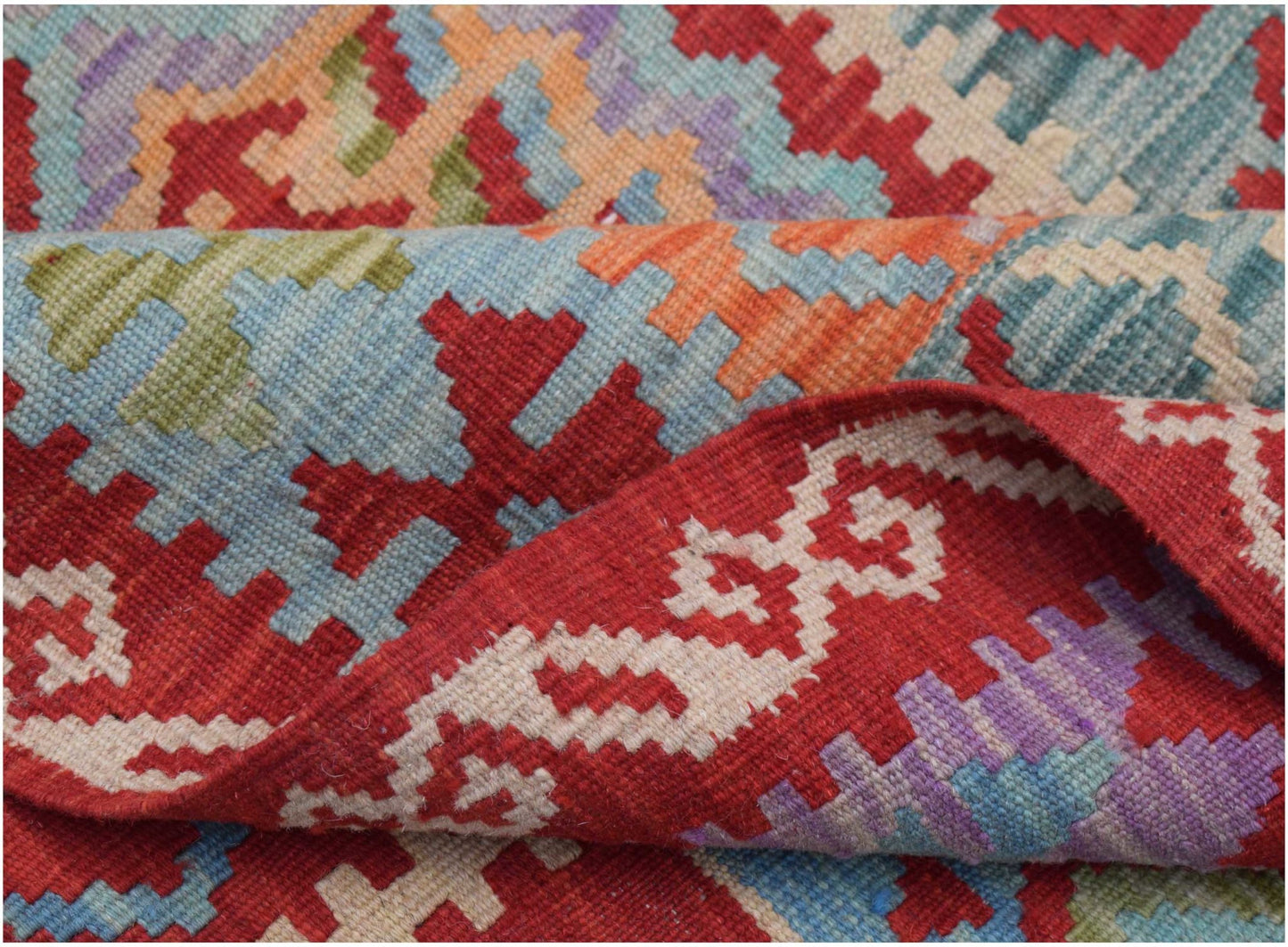 A handwoven Afghan Maimana kilim rug featuring a geometric pattern in red, blue, and orange wool.