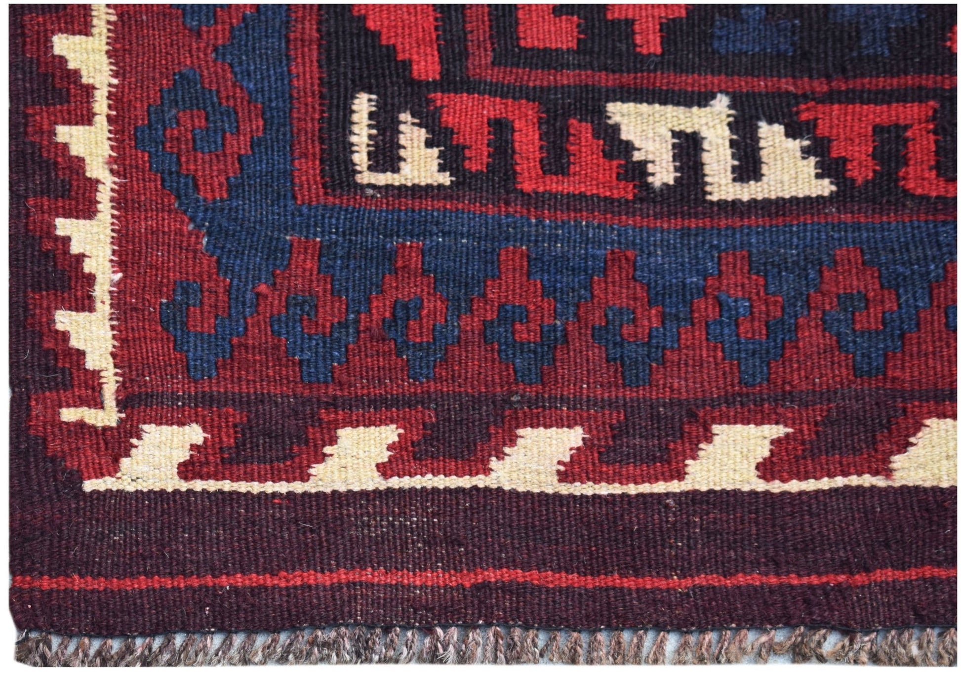 A handmade Afghan Maimana kilim featuring geometric patterns in red, blue, and cream wool.