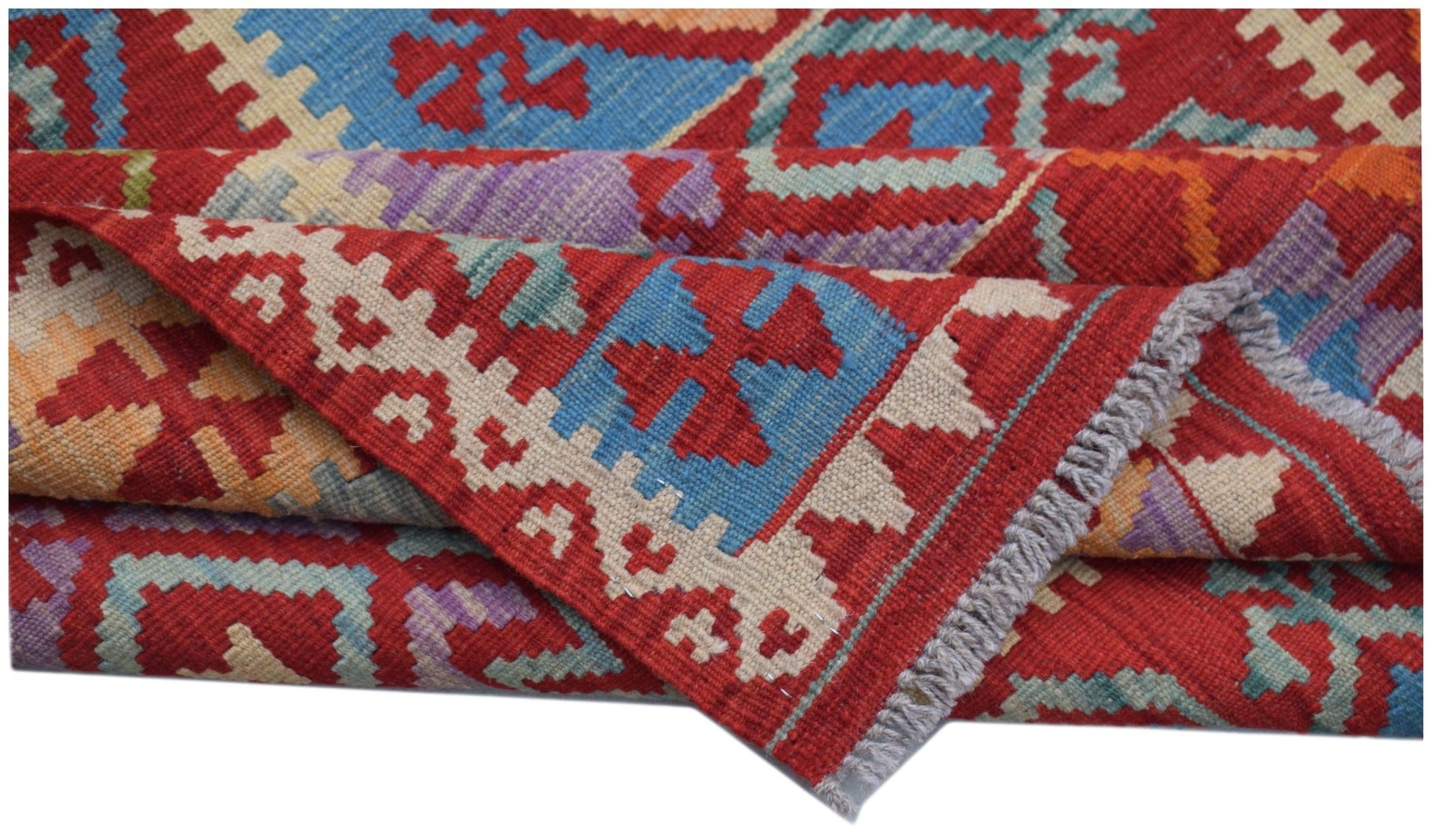A handwoven Afghan Maimana kilim rug featuring geometric patterns in red, blue, and purple wool.