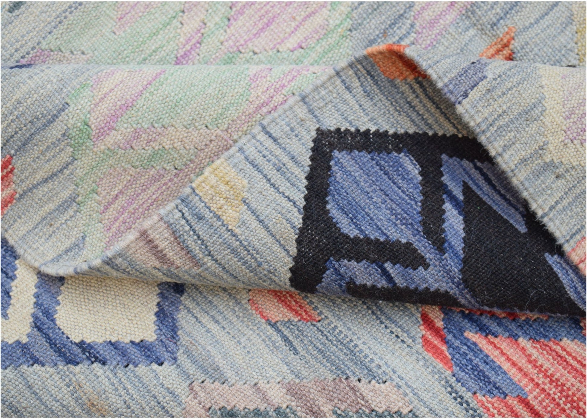 A handwoven Afghan Maimana kilim rug featuring a geometric pattern in blue, red, and cream wool.