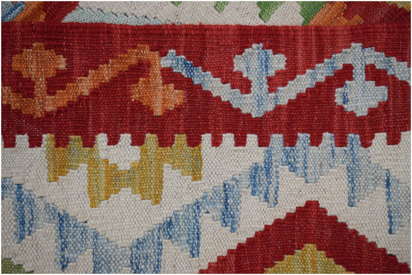 A close-up of a handmade Afghan Maimana kilim featuring geometric patterns in red, blue, and yellow.