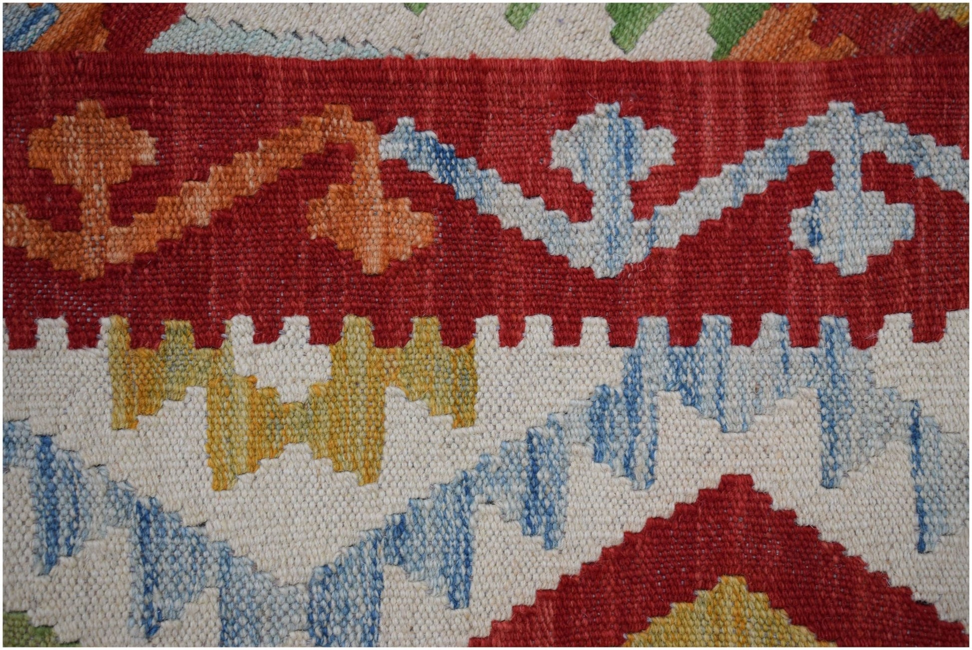 A close-up of a handmade Afghan Maimana kilim featuring geometric patterns in red, blue, and yellow.