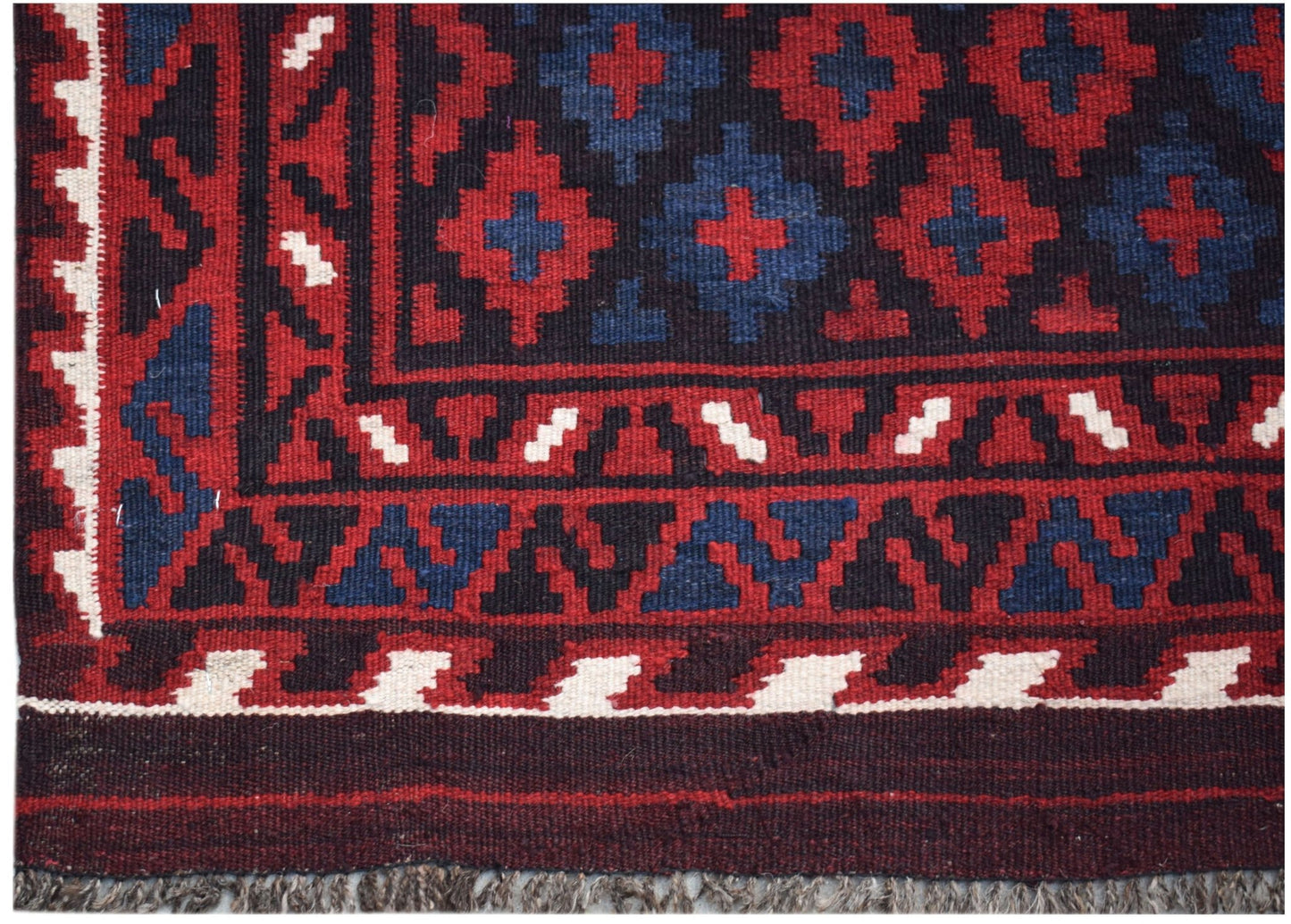 Handwoven Afghan Maimana kilim featuring a geometric pattern in red, blue, and cream wool.