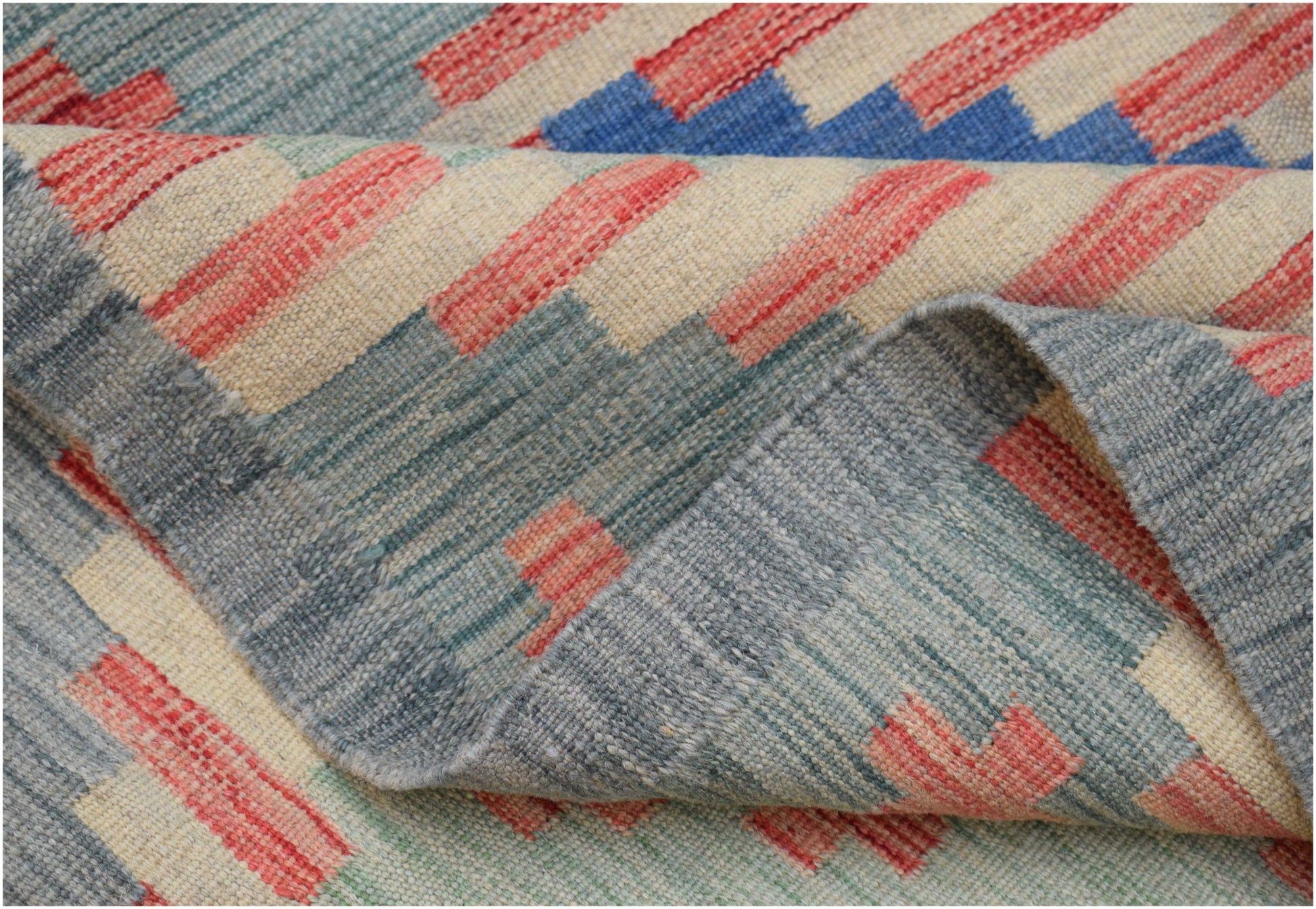 A handwoven Afghan Maimana kilim rug featuring a geometric pattern in blue, red, and cream wool.