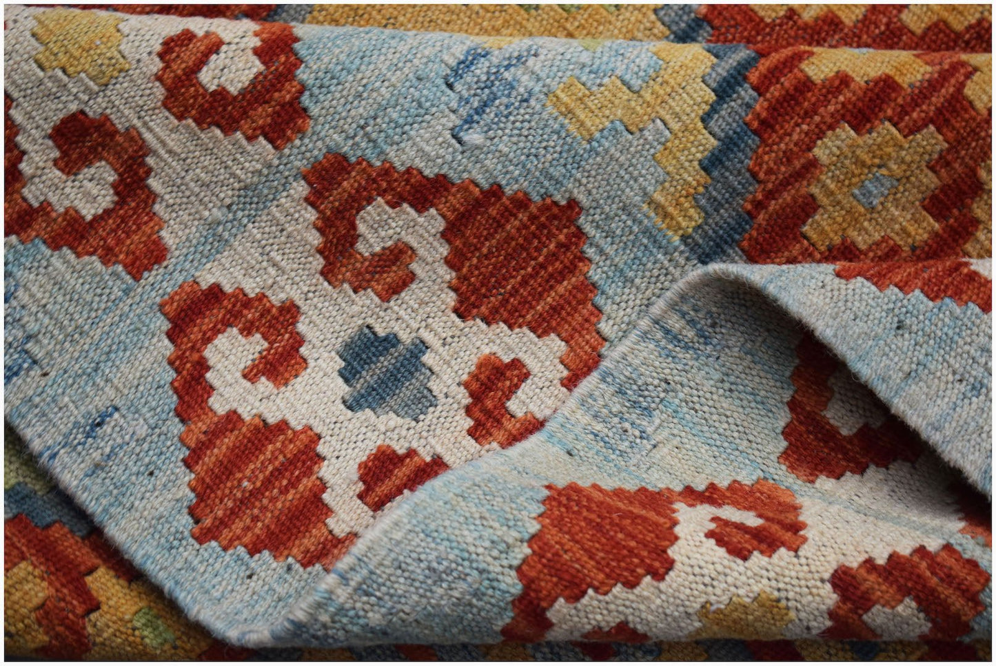 A handmade Afghan Maimana kilim rug featuring a geometric pattern in red, blue, and yellow wool.