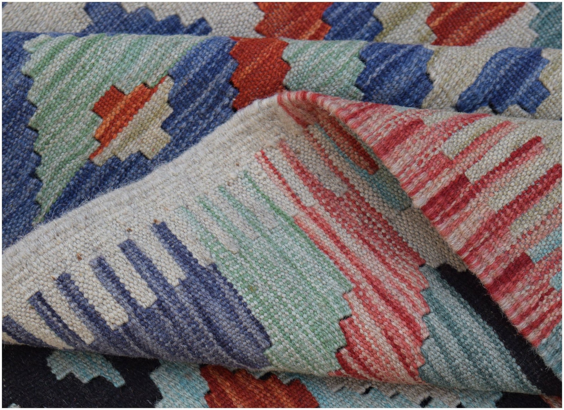 A handwoven Afghan Maimana kilim rug featuring a geometric pattern in vibrant multicolored wool.