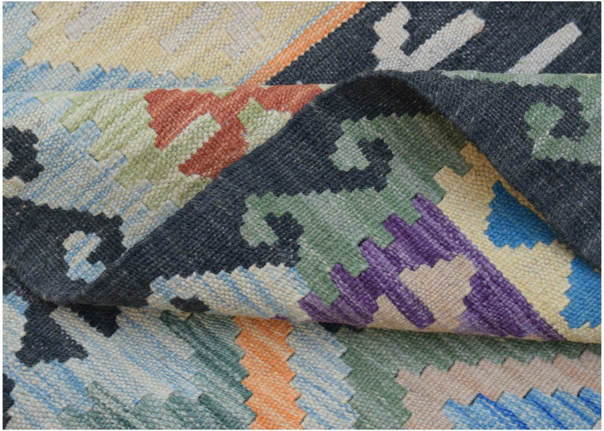 A close-up of a handwoven Afghan Maimana kilim featuring colorful geometric patterns in wool.
