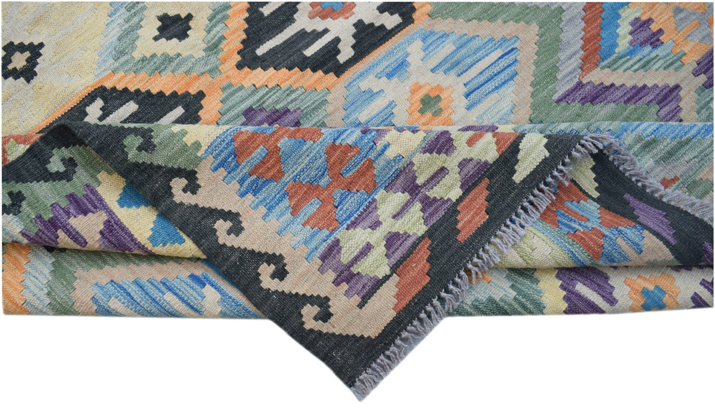 A handwoven Afghan Maimana kilim rug featuring a colorful geometric pattern and fringed edges.