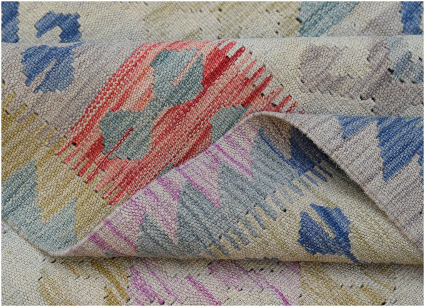 A handwoven Afghan Maimana kilim rug featuring a geometric pattern in muted, multicolored tones.