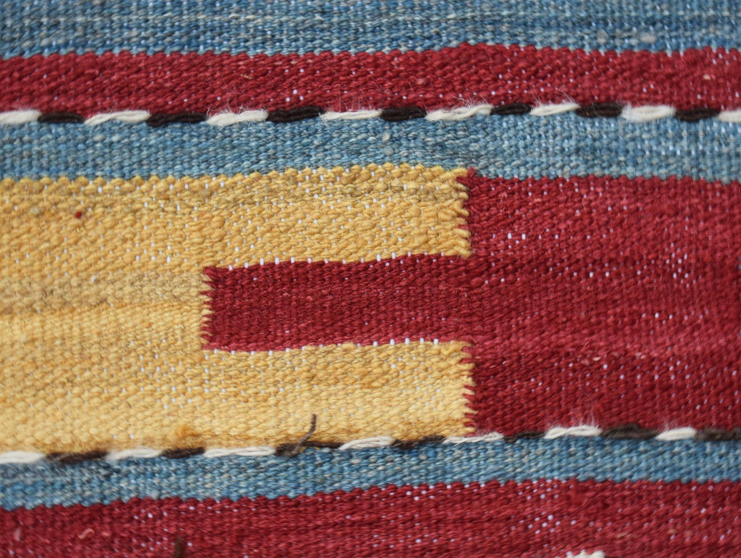 A close-up of a handmade Afghan Maimana kilim featuring geometric patterns in red, yellow, and blue.