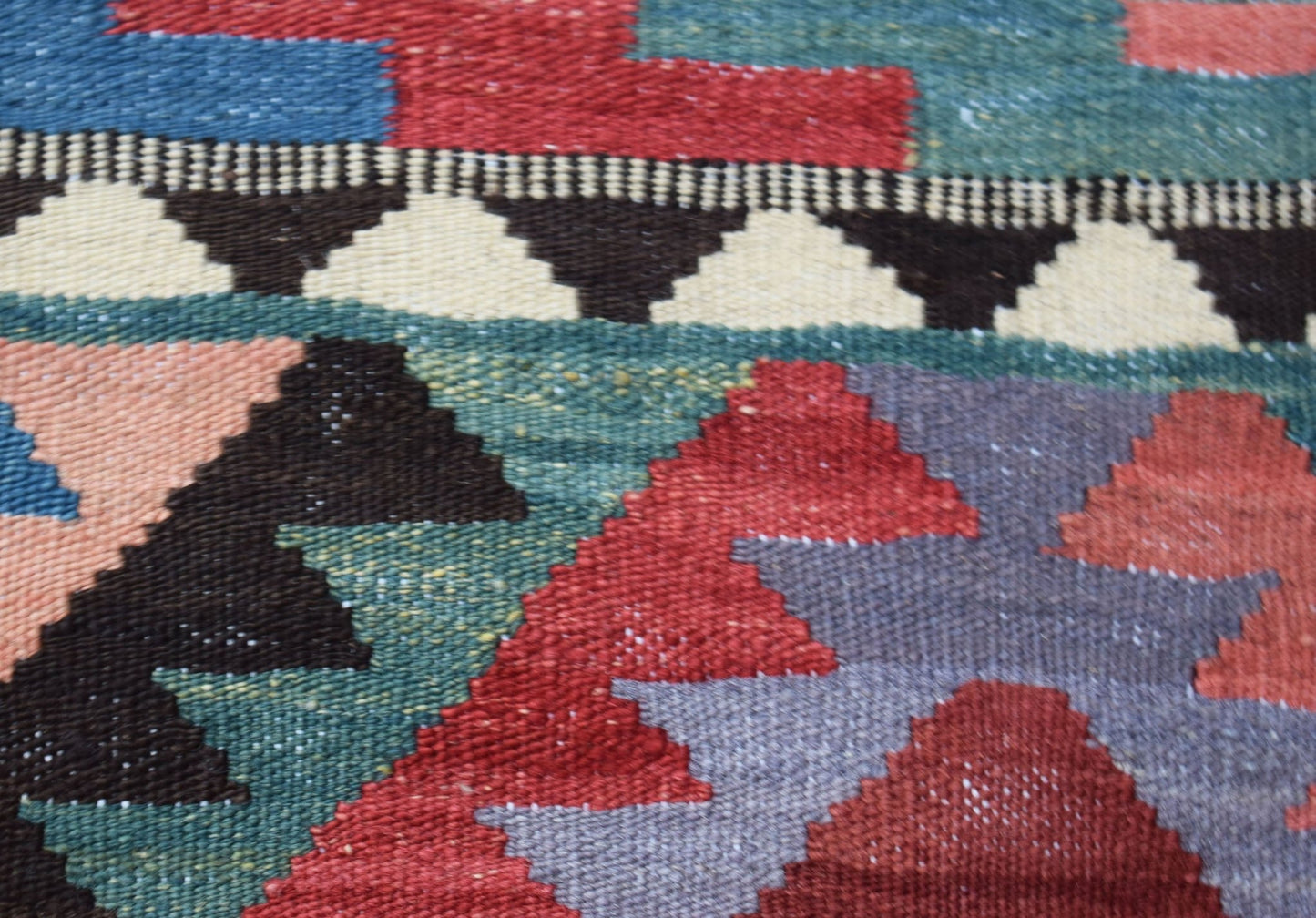 A close-up of a handmade Afghan Maimana kilim featuring geometric patterns in red, blue, and green.