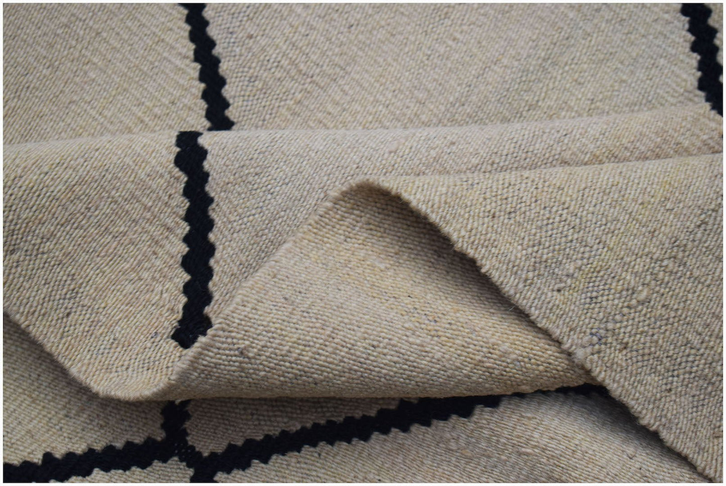 A handwoven Afghan Maimana kilim rug featuring a beige wool base with black geometric lines.