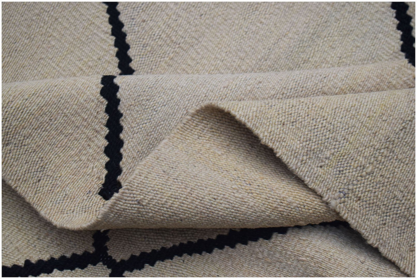 A handwoven Afghan Maimana kilim rug featuring a beige wool base with black geometric lines.