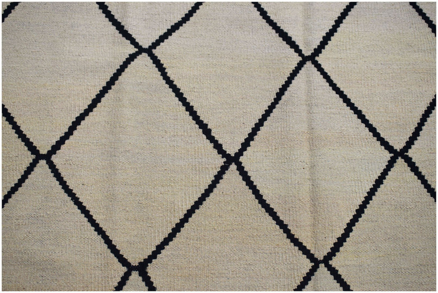 A beige kilim rug with a black diamond pattern.