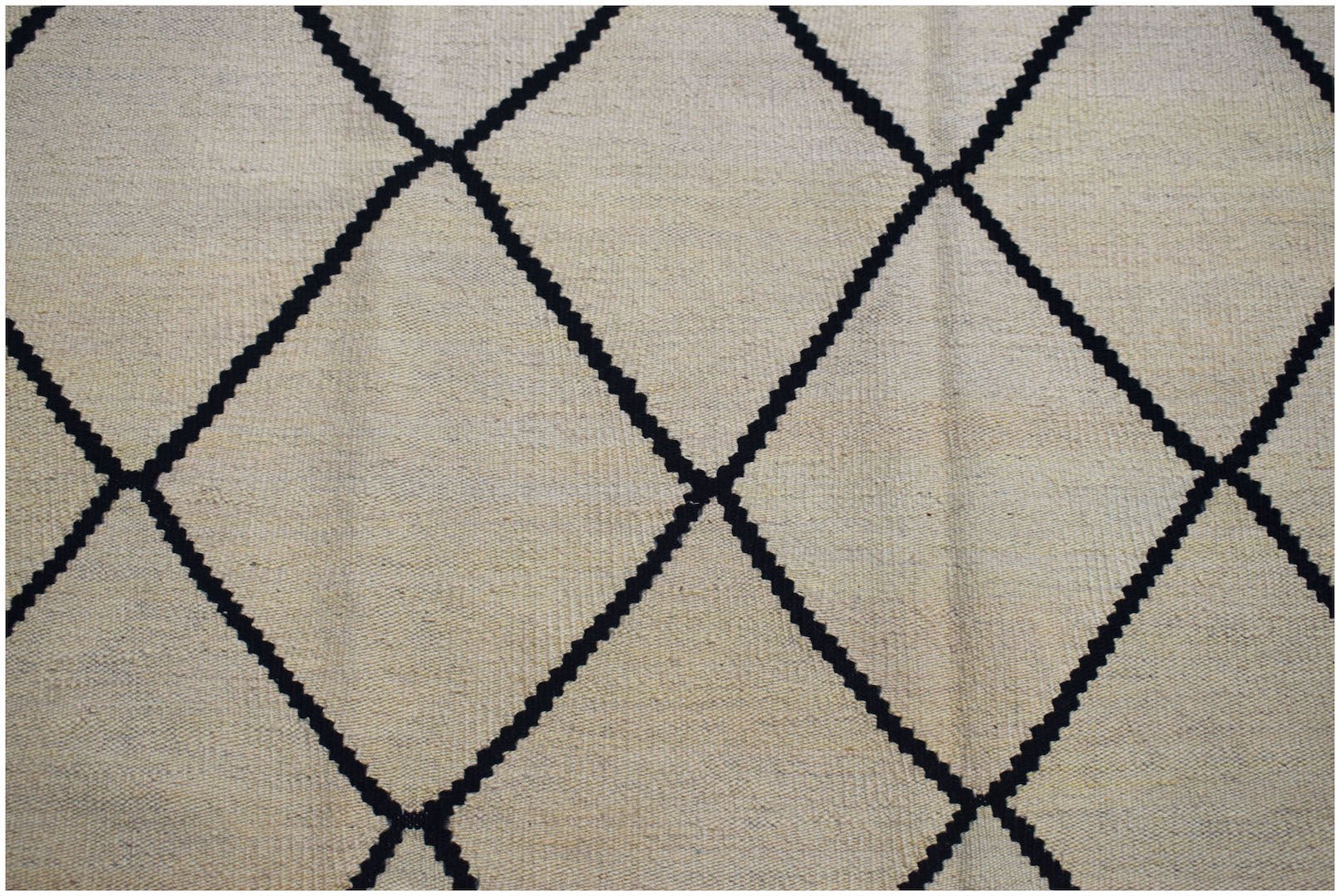 A beige kilim rug with a black diamond pattern.