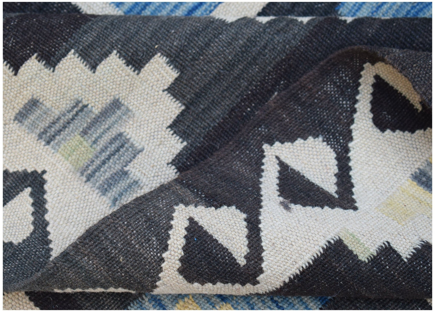 A handmade Afghan Maimana kilim rug featuring a geometric pattern in black, white, and blue.