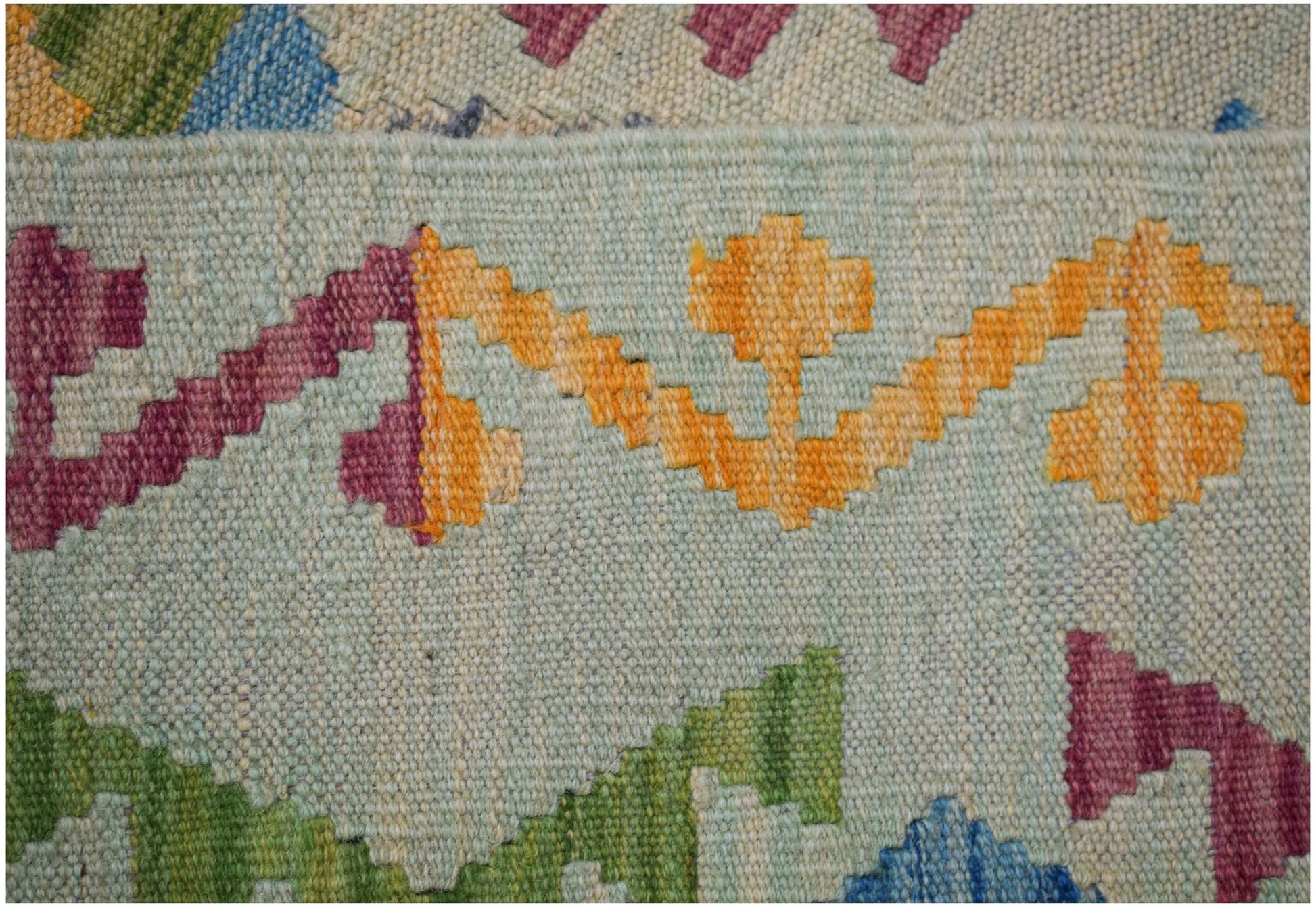 A close-up of a handmade Afghan Maimana kilim featuring geometric patterns in vibrant wool colors.