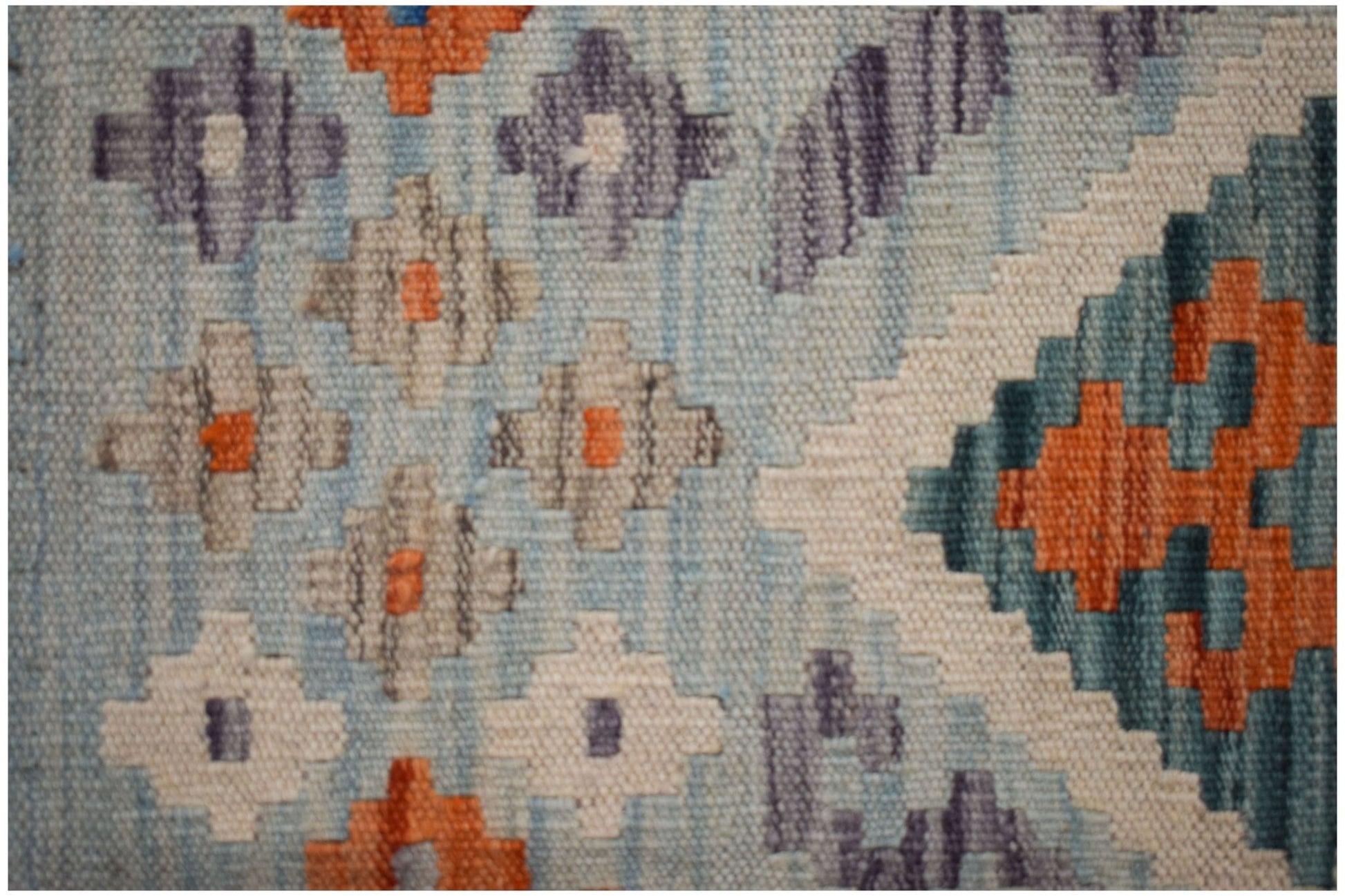 A close-up of a handmade Afghan Maimana kilim featuring geometric patterns in blue, orange, and grey.