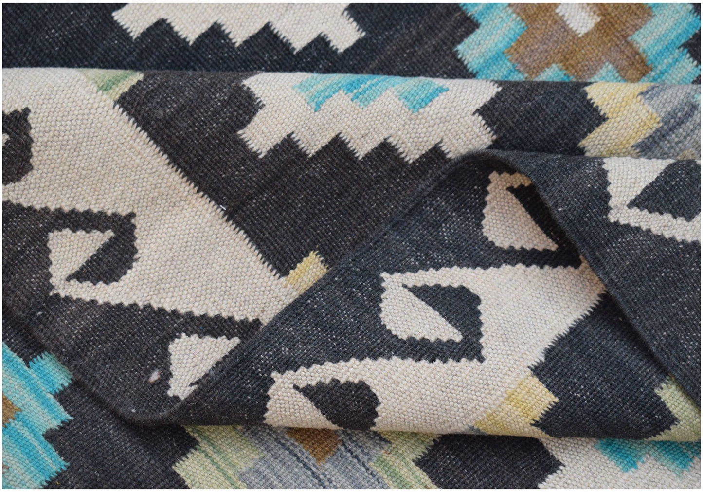 A handmade Afghan Maimana kilim rug featuring a geometric pattern in black, white, and blue tones.