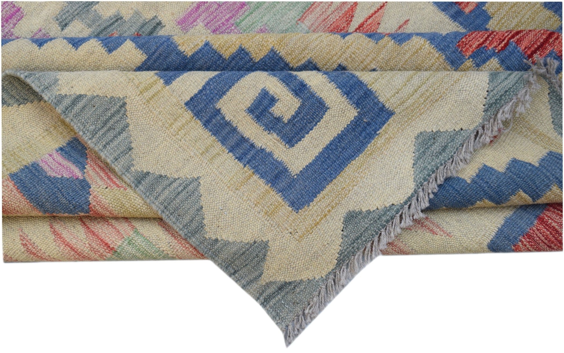 A folded Afghan Maimana kilim rug featuring a geometric blue spiral pattern on a cream background.