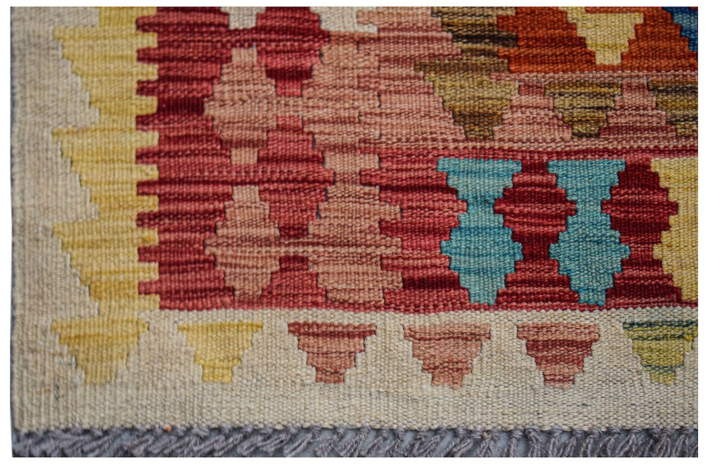 A close-up of a handmade Afghan Maimana kilim featuring geometric patterns in red, blue, and yellow.