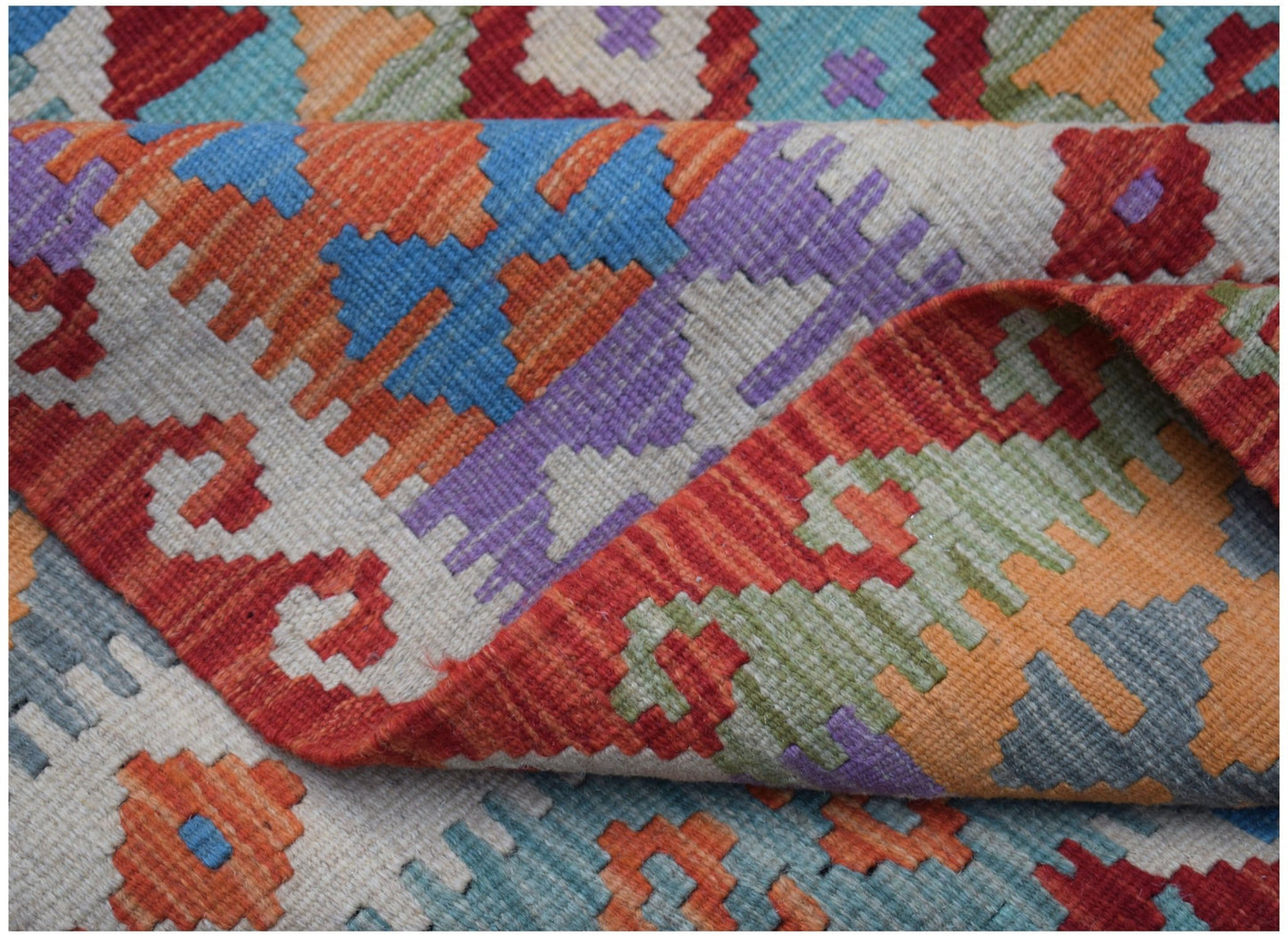 A handmade Afghan Maimana kilim rug featuring a colorful geometric pattern on a flatweave wool base.