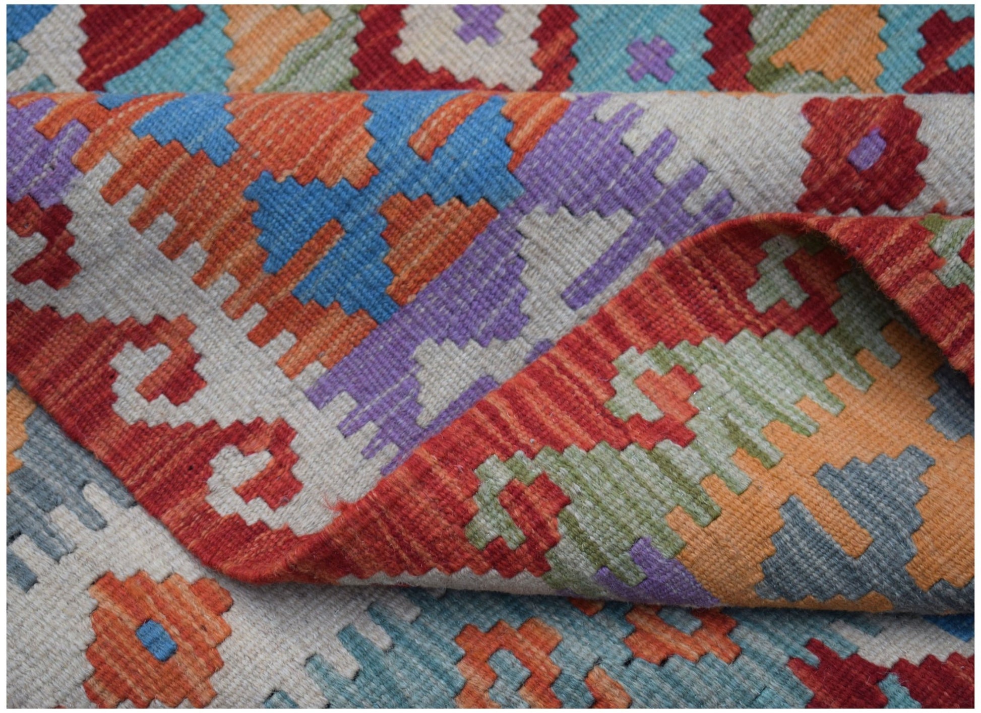 A handmade Afghan Maimana kilim rug featuring a colorful geometric pattern on a flatweave wool base.