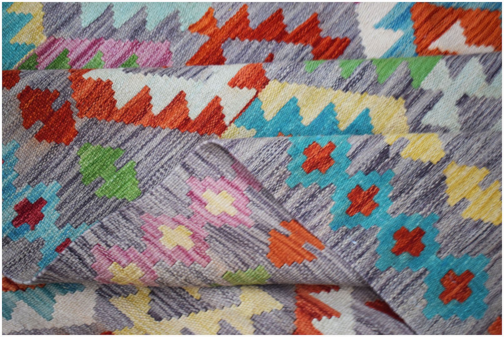 Handwoven Afghan Maimana kilim rug featuring a colorful geometric pattern on a grey background.