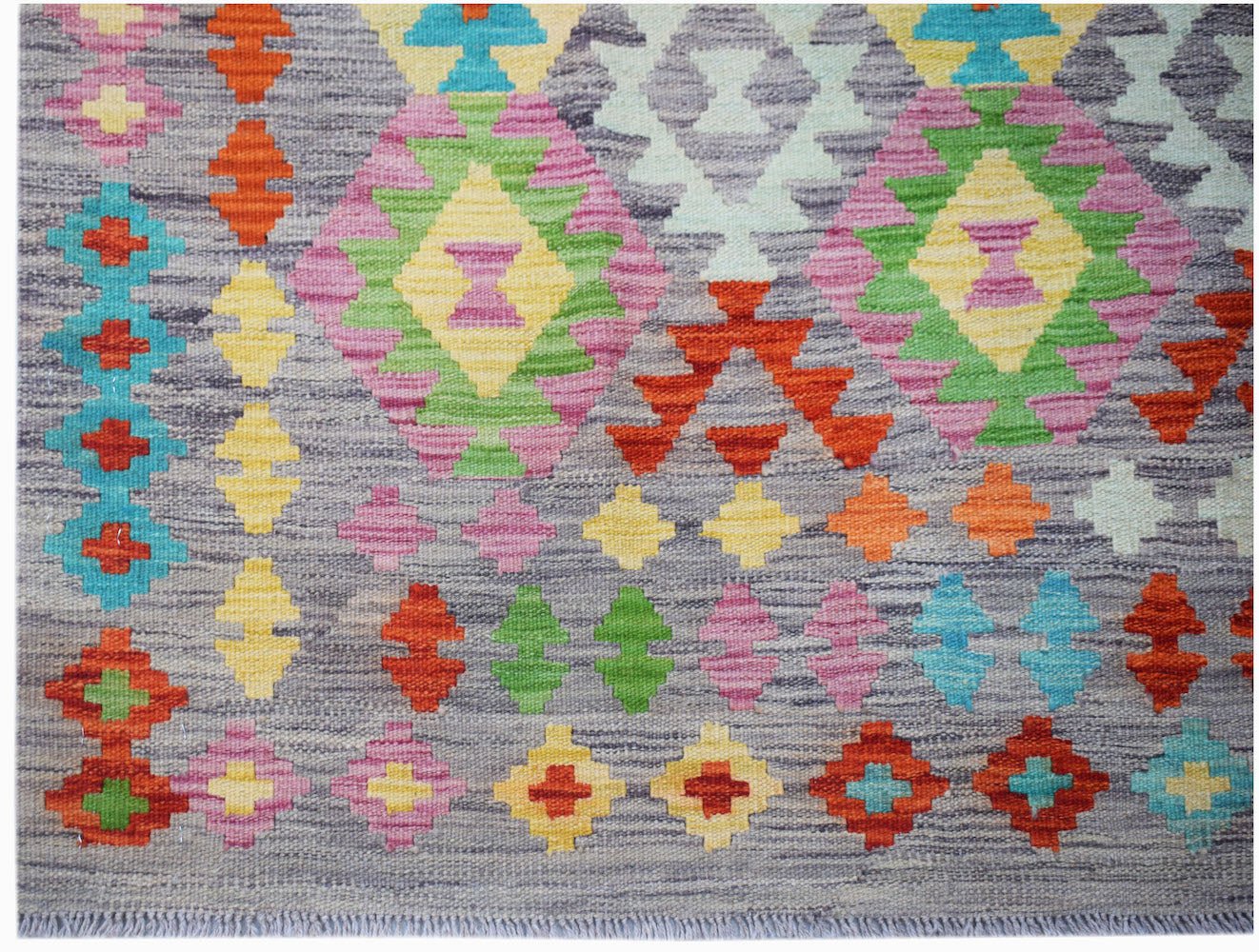 Afghan Maimana Kilim with geometric diamond patterns in multiple colors on a gray background.