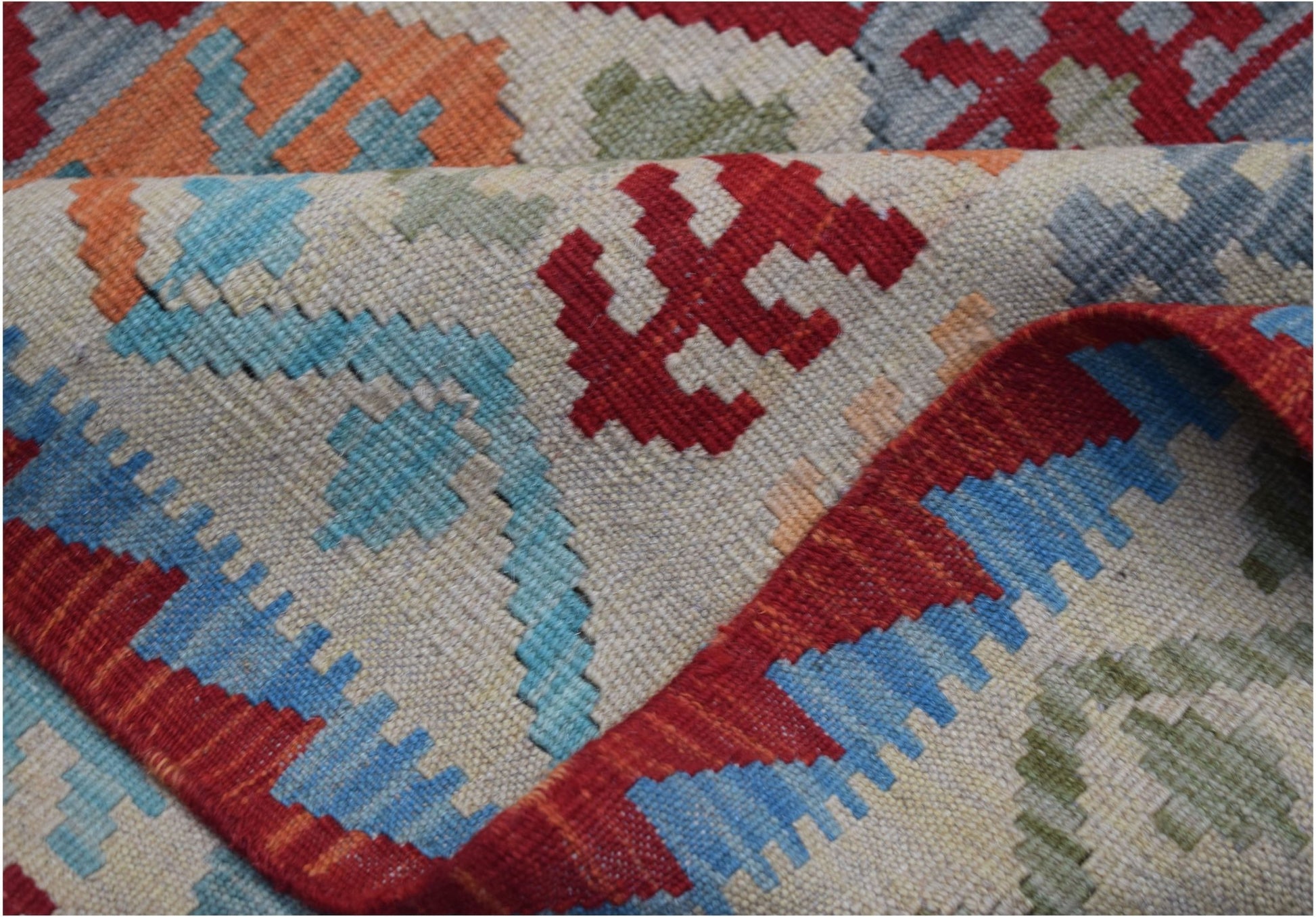 A handmade Afghan Maimana kilim rug featuring a geometric pattern in red, blue, and orange wool.