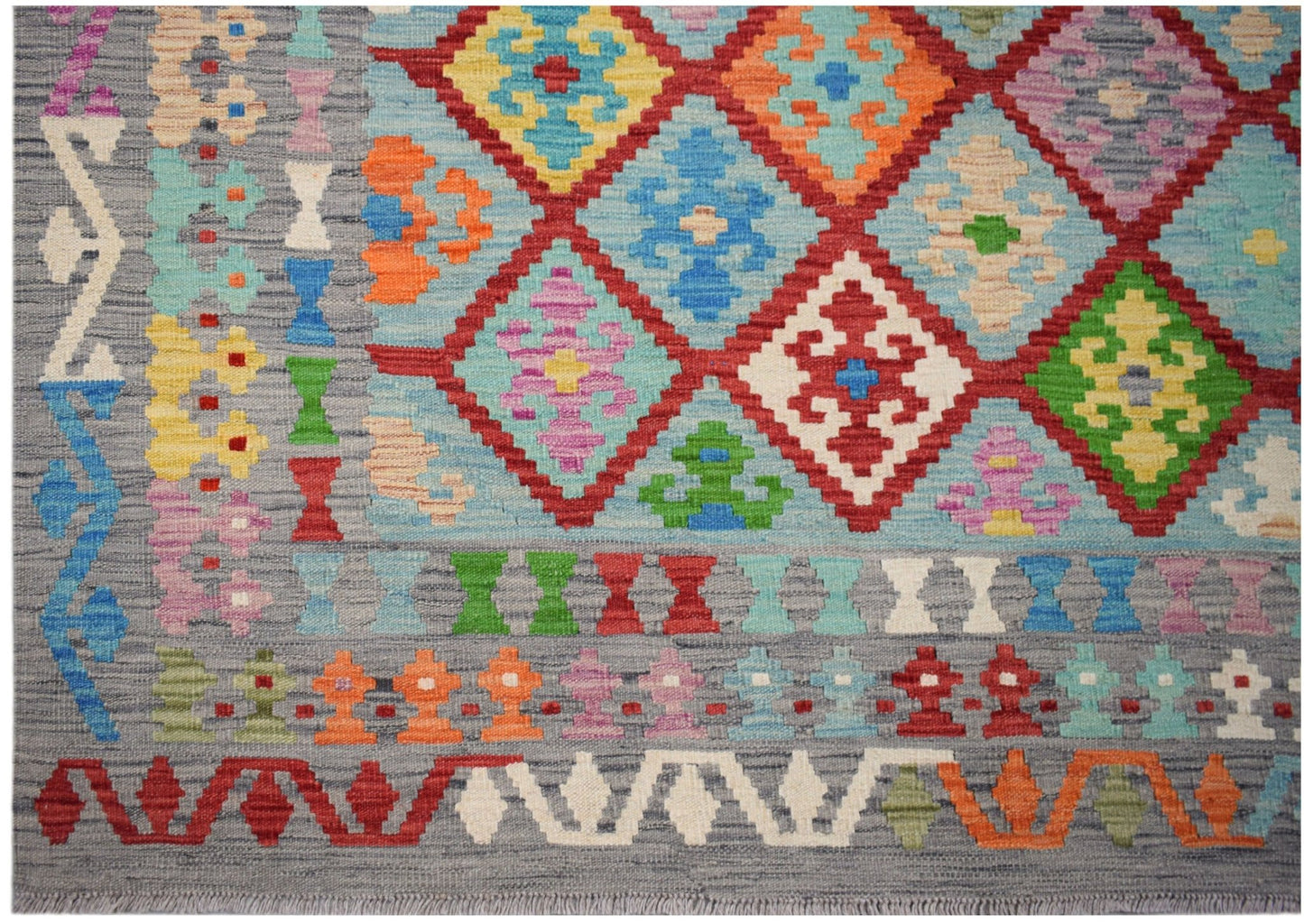 Handwoven Afghan Maimana kilim featuring a colorful geometric diamond pattern on a grey background.