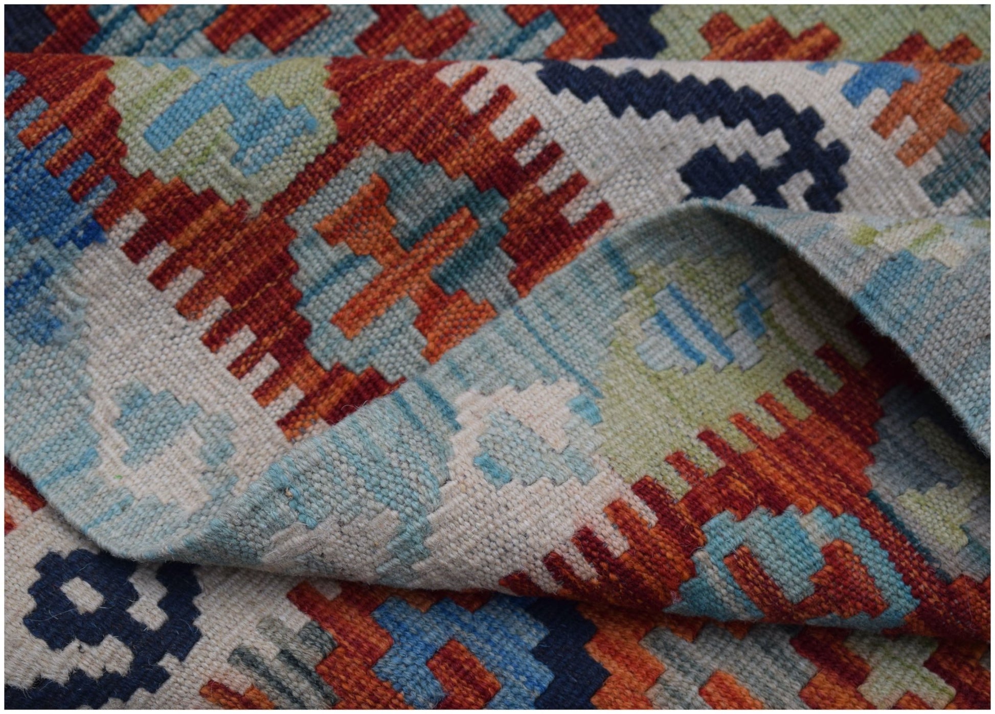 A handwoven Afghan Maimana kilim featuring a geometric pattern in red, blue, and green wool.