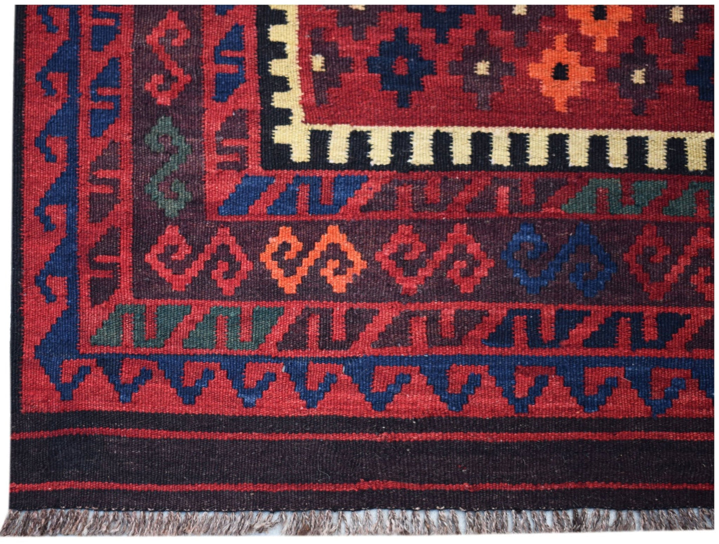 Handwoven Afghan Maimana kilim featuring geometric patterns in red, blue, and orange wool.