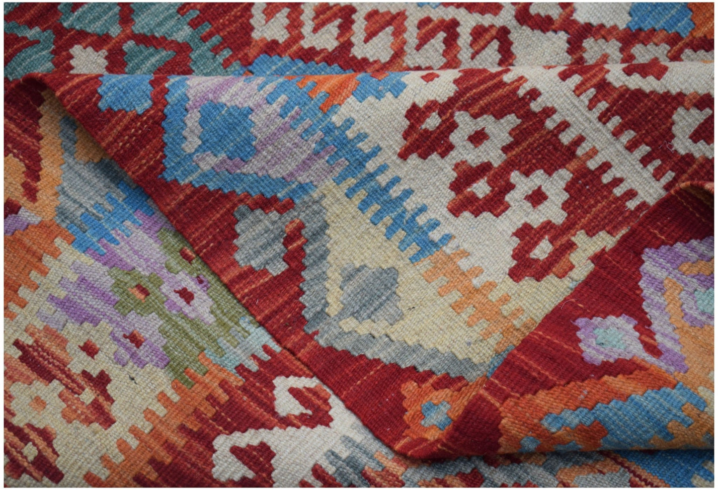 A handwoven Afghan Maimana kilim rug featuring a vibrant geometric pattern in wool.