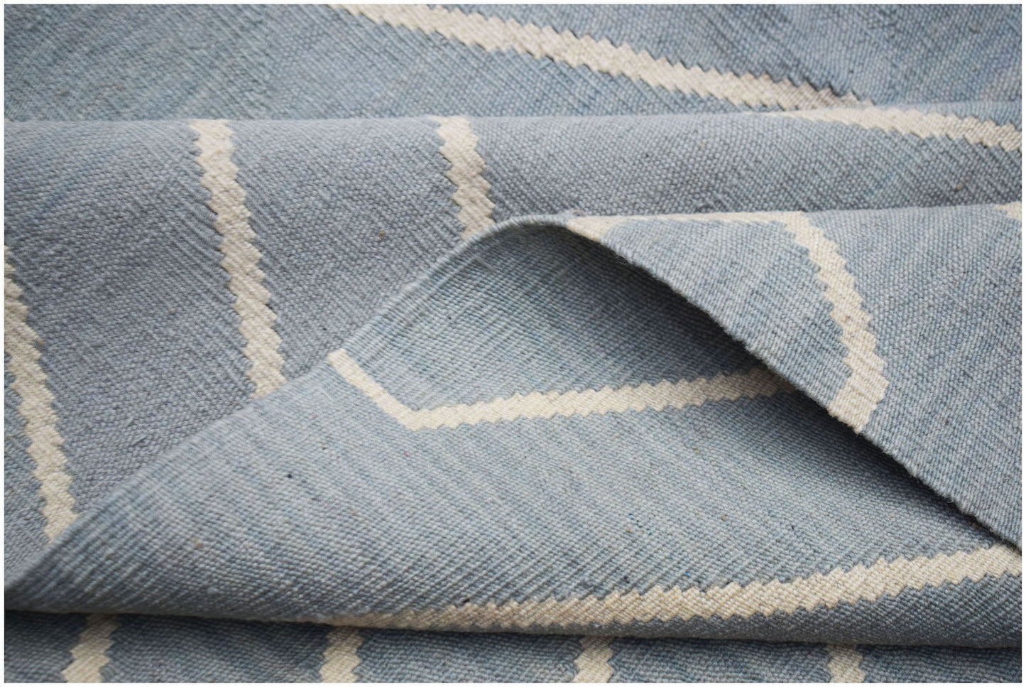 A handwoven Afghan Maimana kilim rug featuring a light blue field with cream geometric stripes.