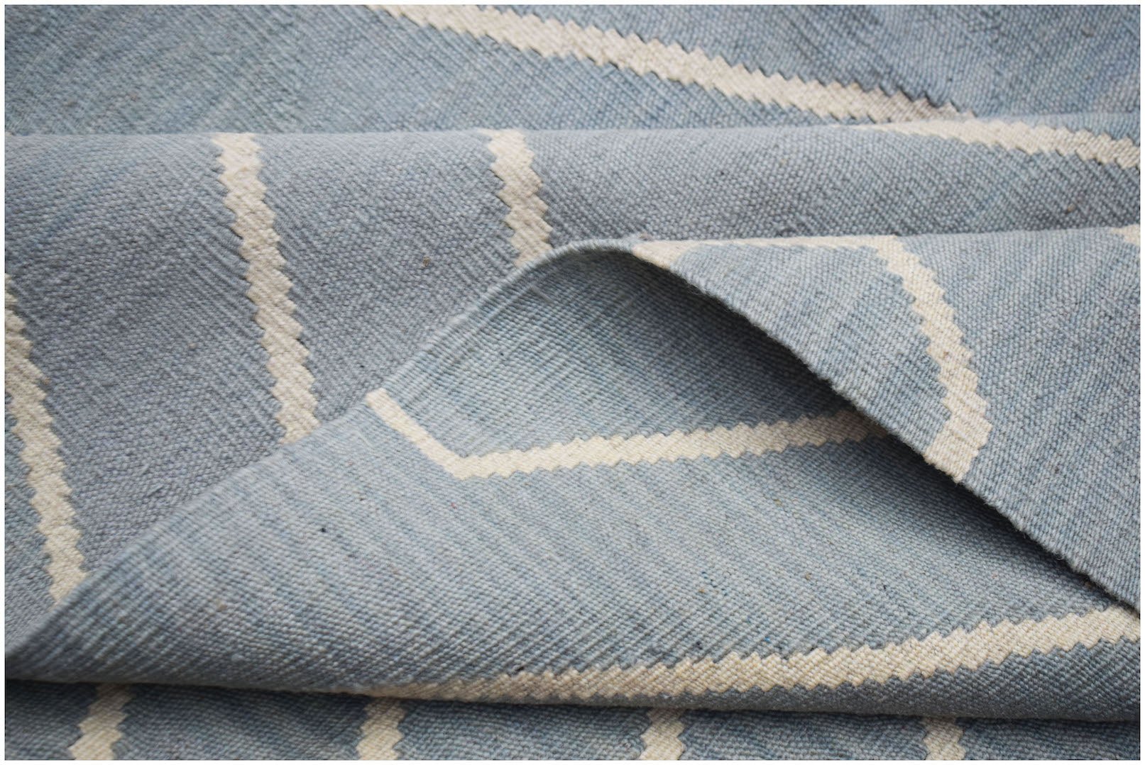 A handwoven Afghan Maimana kilim rug featuring a light blue field with cream geometric stripes.