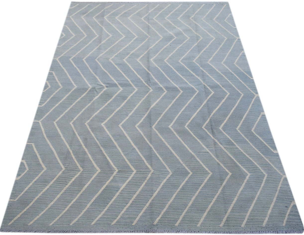 A handmade Afghan Maimana kilim rug featuring a light blue field with a white chevron pattern.