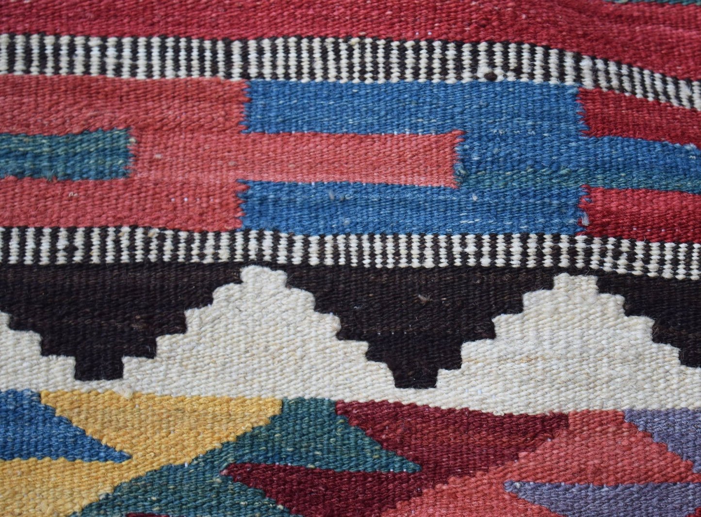 A close-up of a handmade Afghan Maimana kilim featuring geometric patterns in wool.