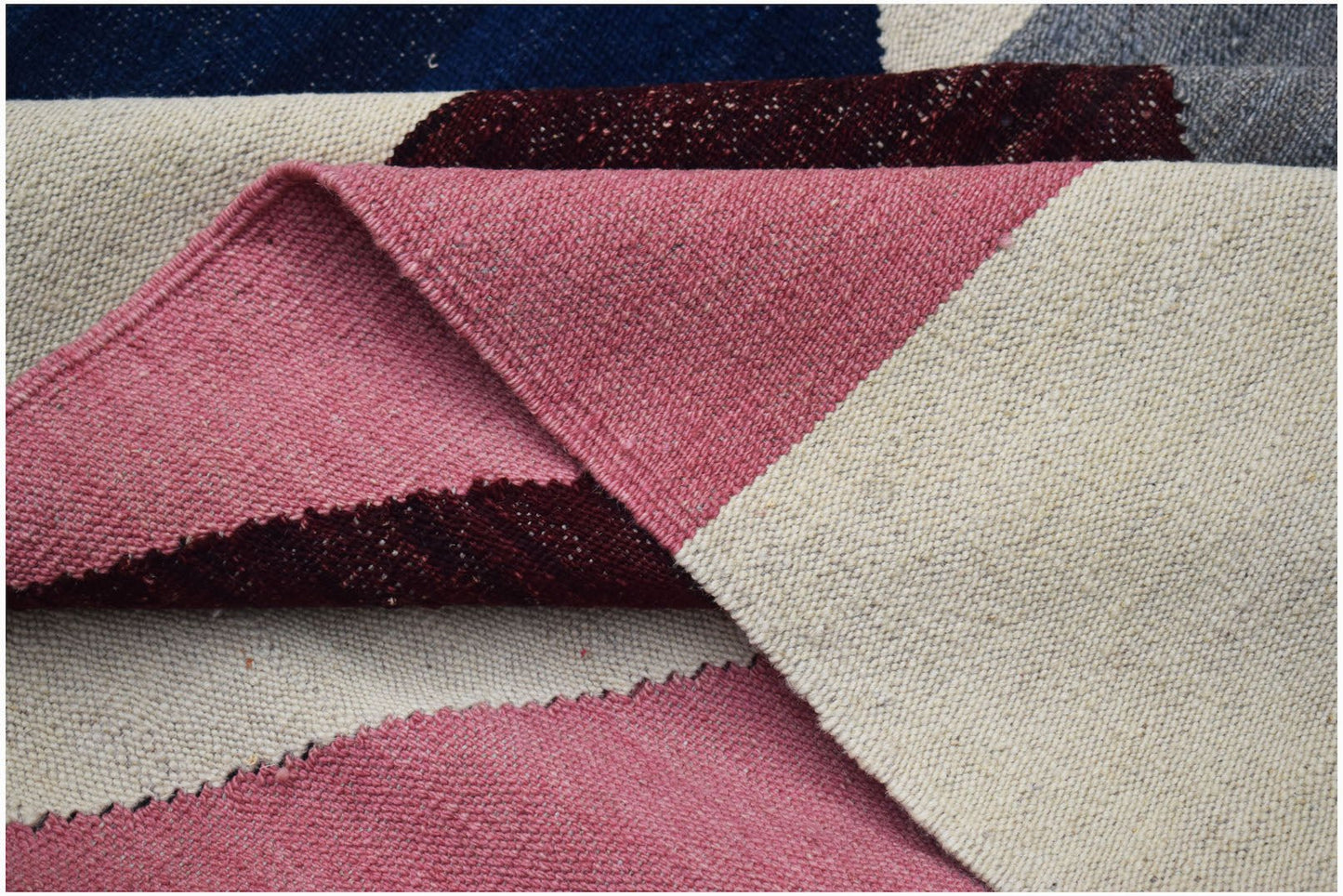 A handwoven Afghan Maimana kilim featuring a geometric pattern in pink, cream, and dark red wool.