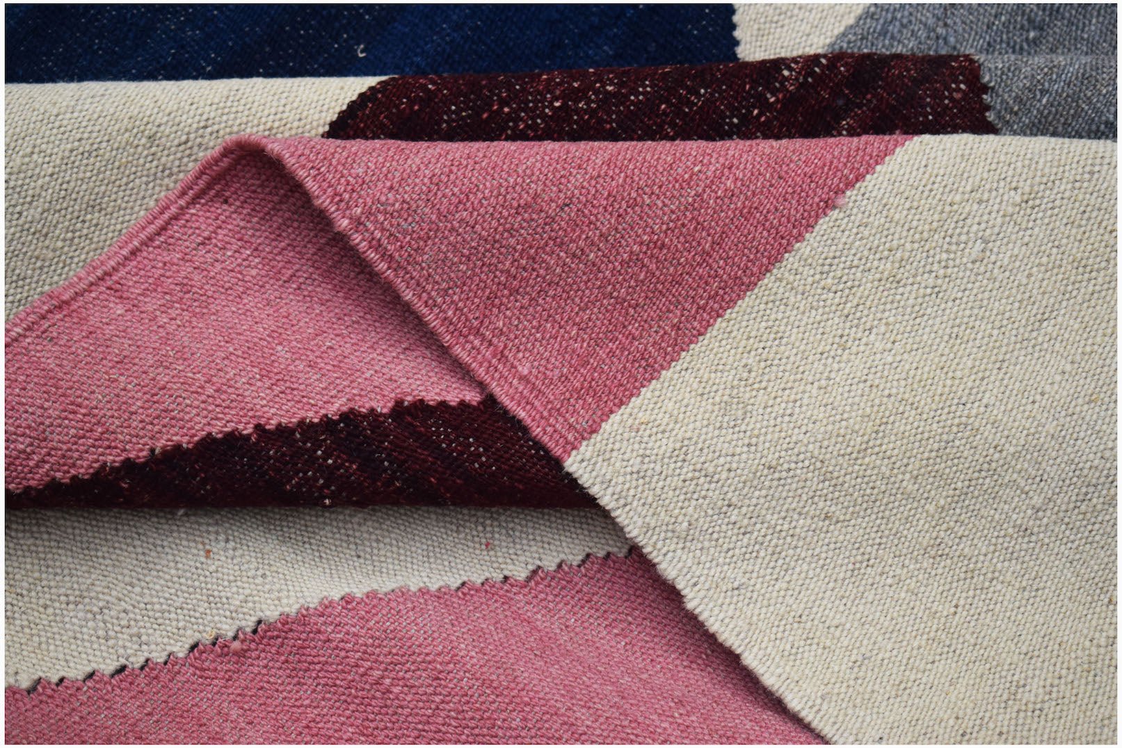 A handwoven Afghan Maimana kilim featuring a geometric pattern in pink, cream, and dark red wool.
