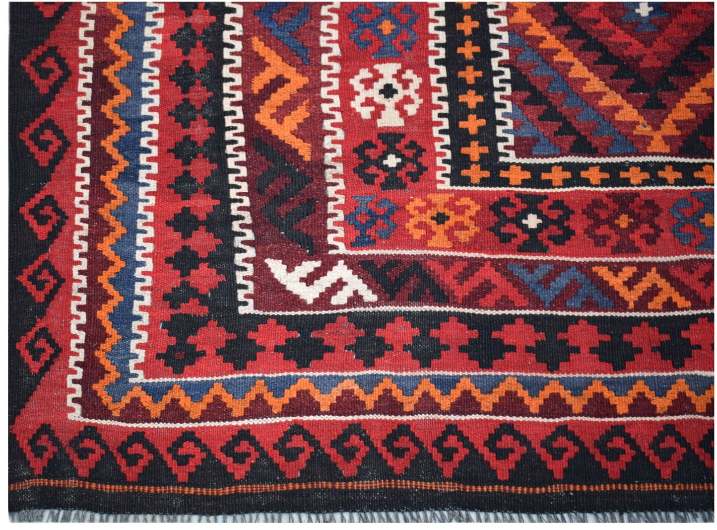 A handmade Afghan Maimana kilim featuring intricate geometric patterns in red, blue, and orange.