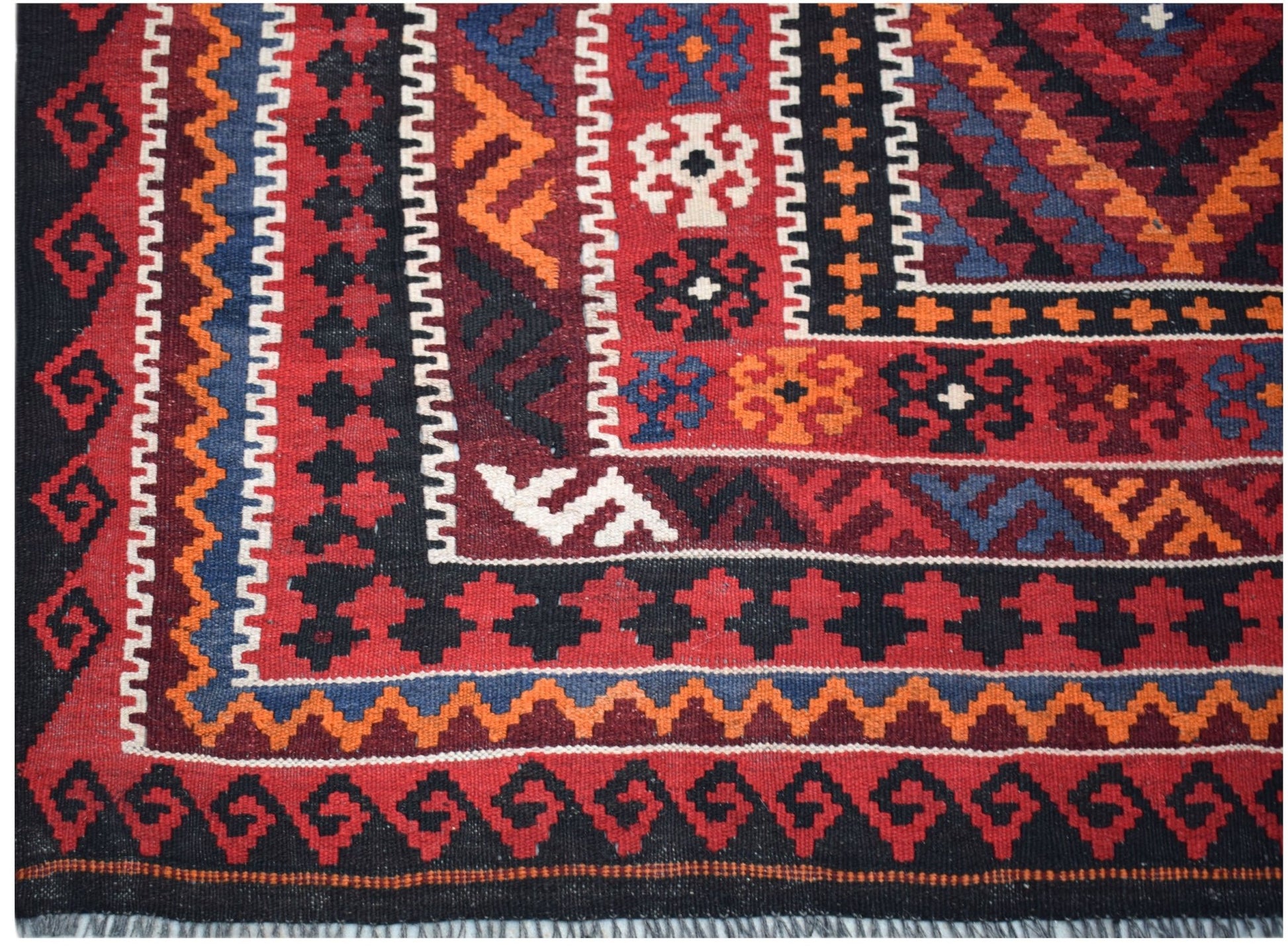 A handmade Afghan Maimana kilim featuring intricate geometric patterns in red, blue, and orange.